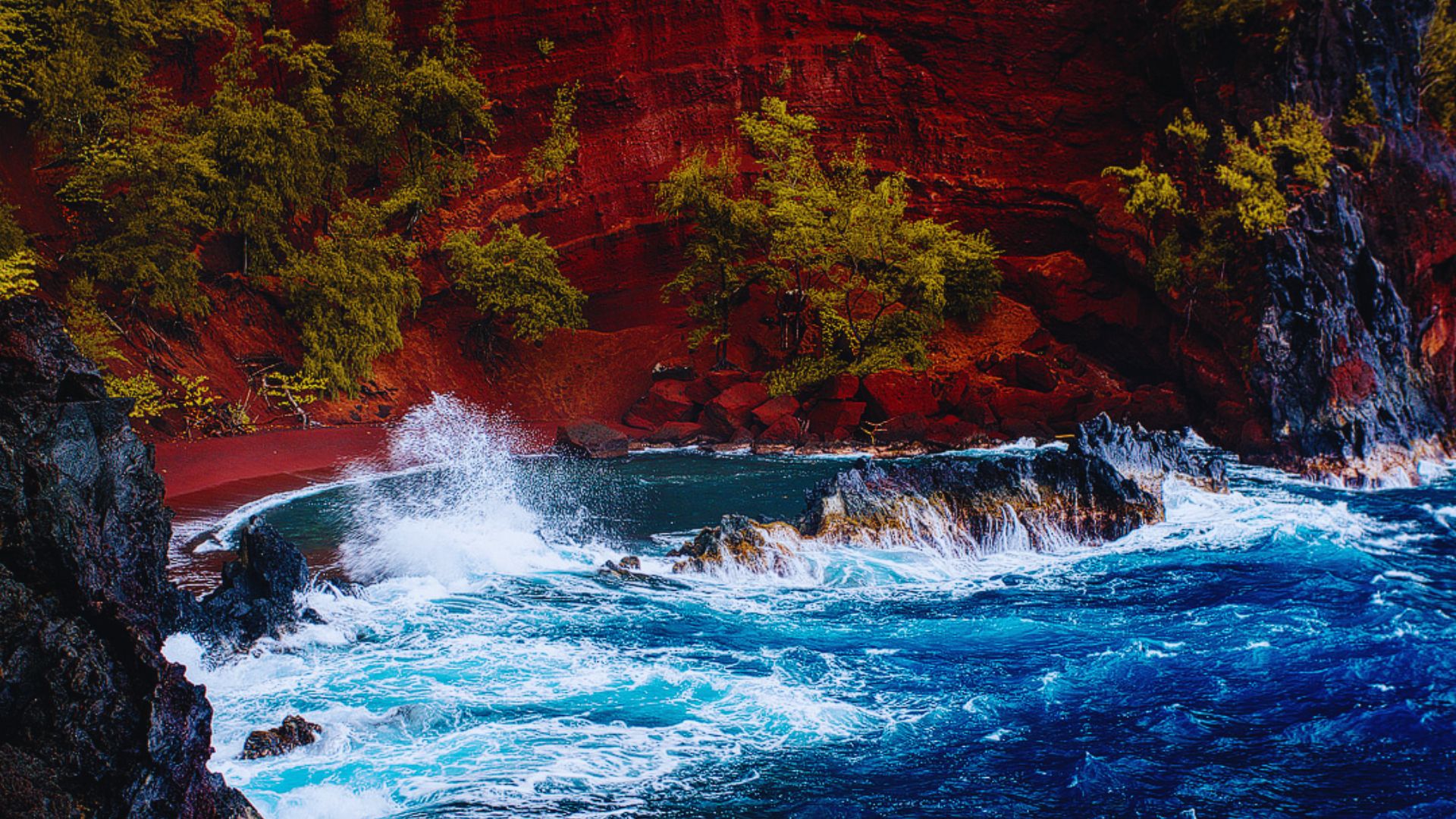 A stunning ocean scene featuring red sand and clear blue water under a bright sky.