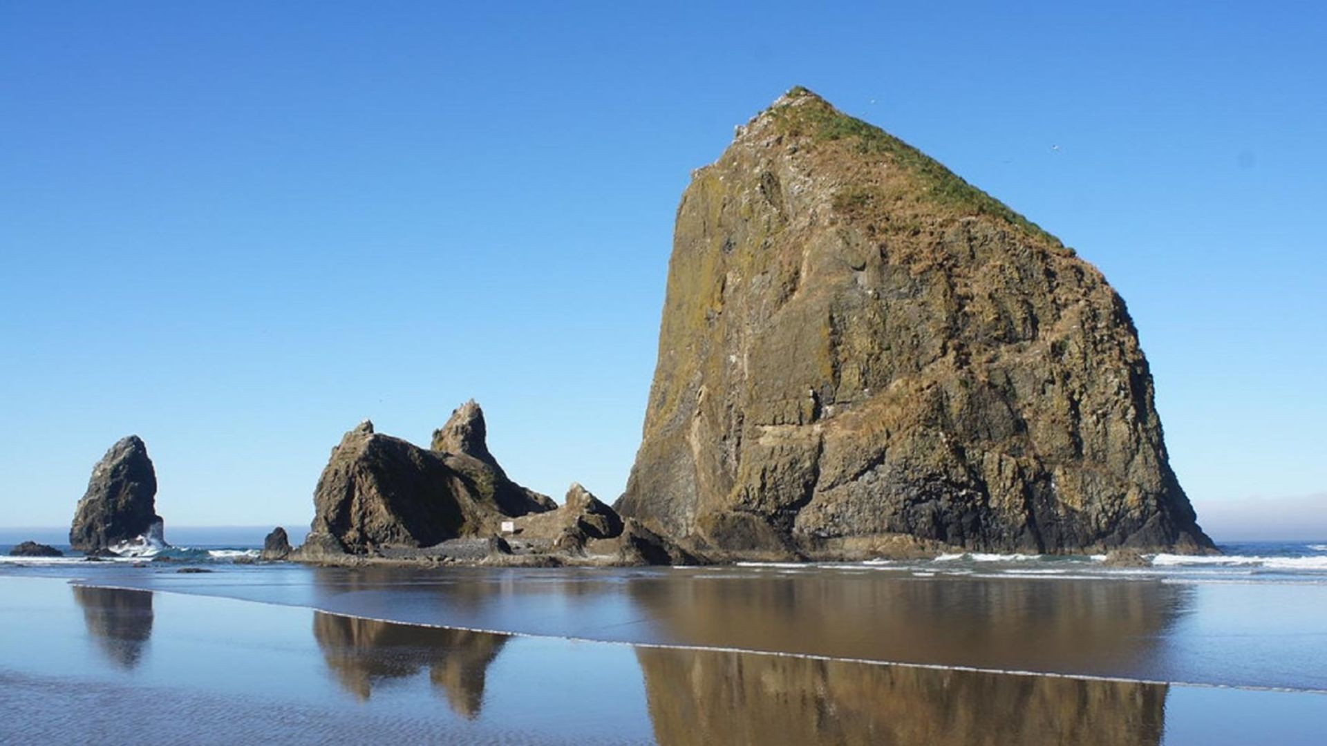 Haystack Rock rises majestically at Cannon Beach, Oregon, surrounded by sandy shores and gentle ocean waves.