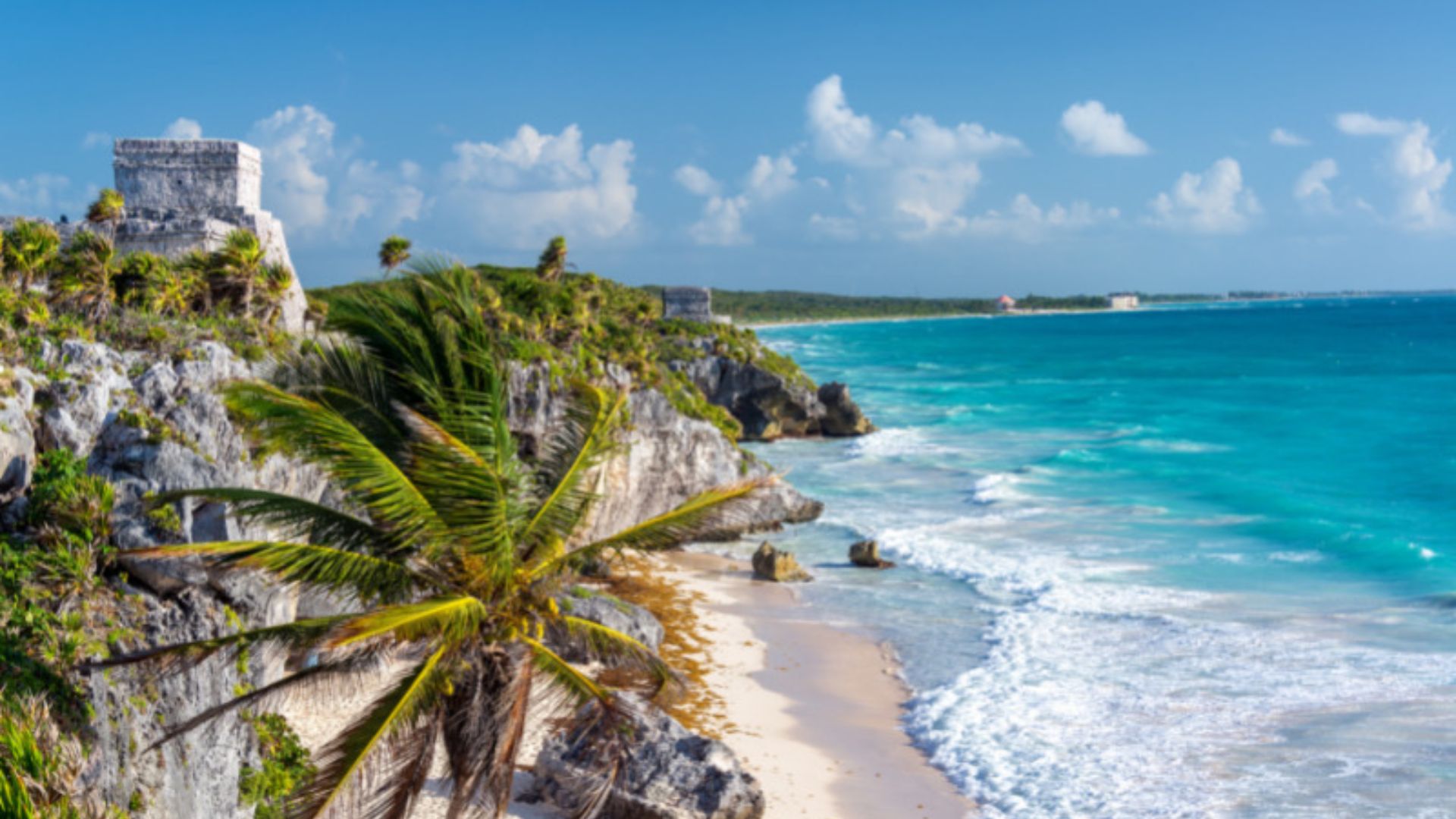 Scenic view of Tulum, Mexico, featuring lush greenery and ancient Mayan ruins against a clear blue sky.