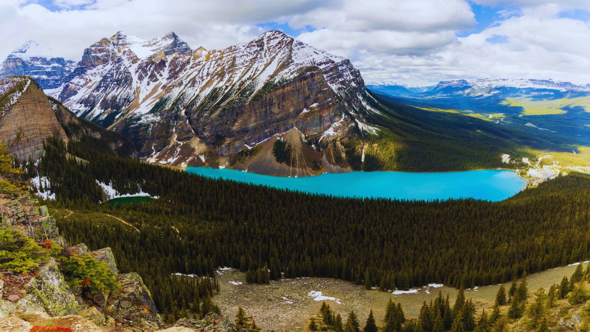 A serene mountain lake nestled among lush trees and towering mountains under a clear blue sky.