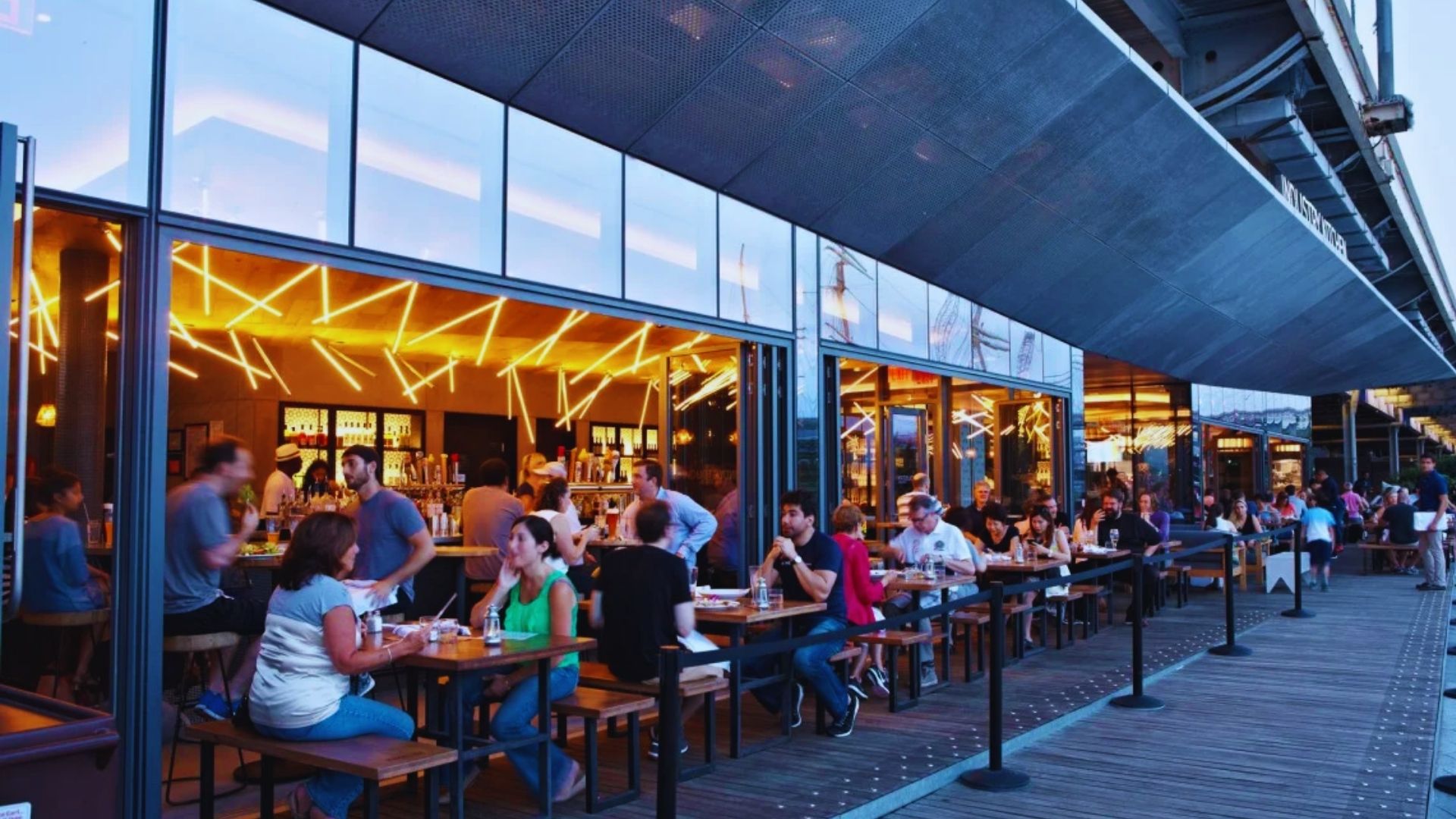 1. A bustling restaurant patio with diners enjoying meals at tables under umbrellas on a sunny day.