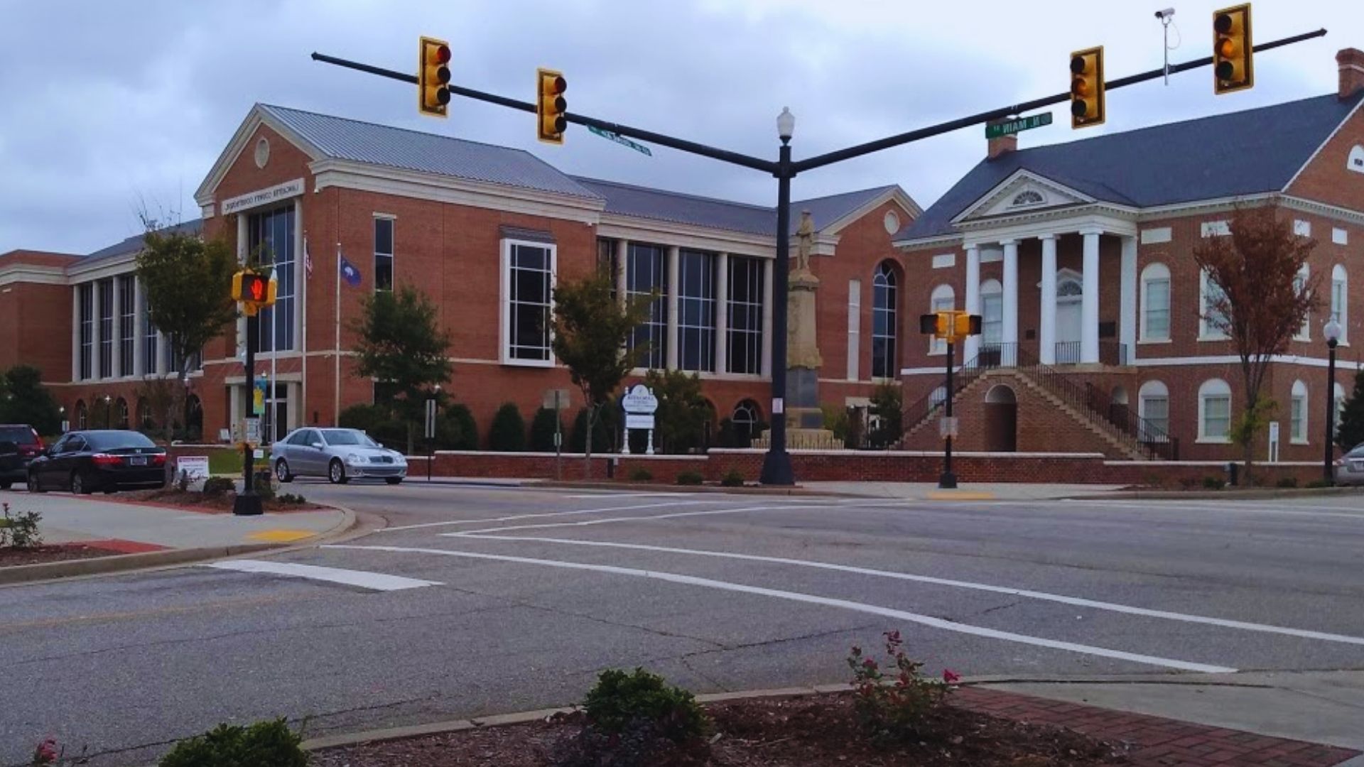 A red brick building stands beside a traffic light, with a car passing by on the street.