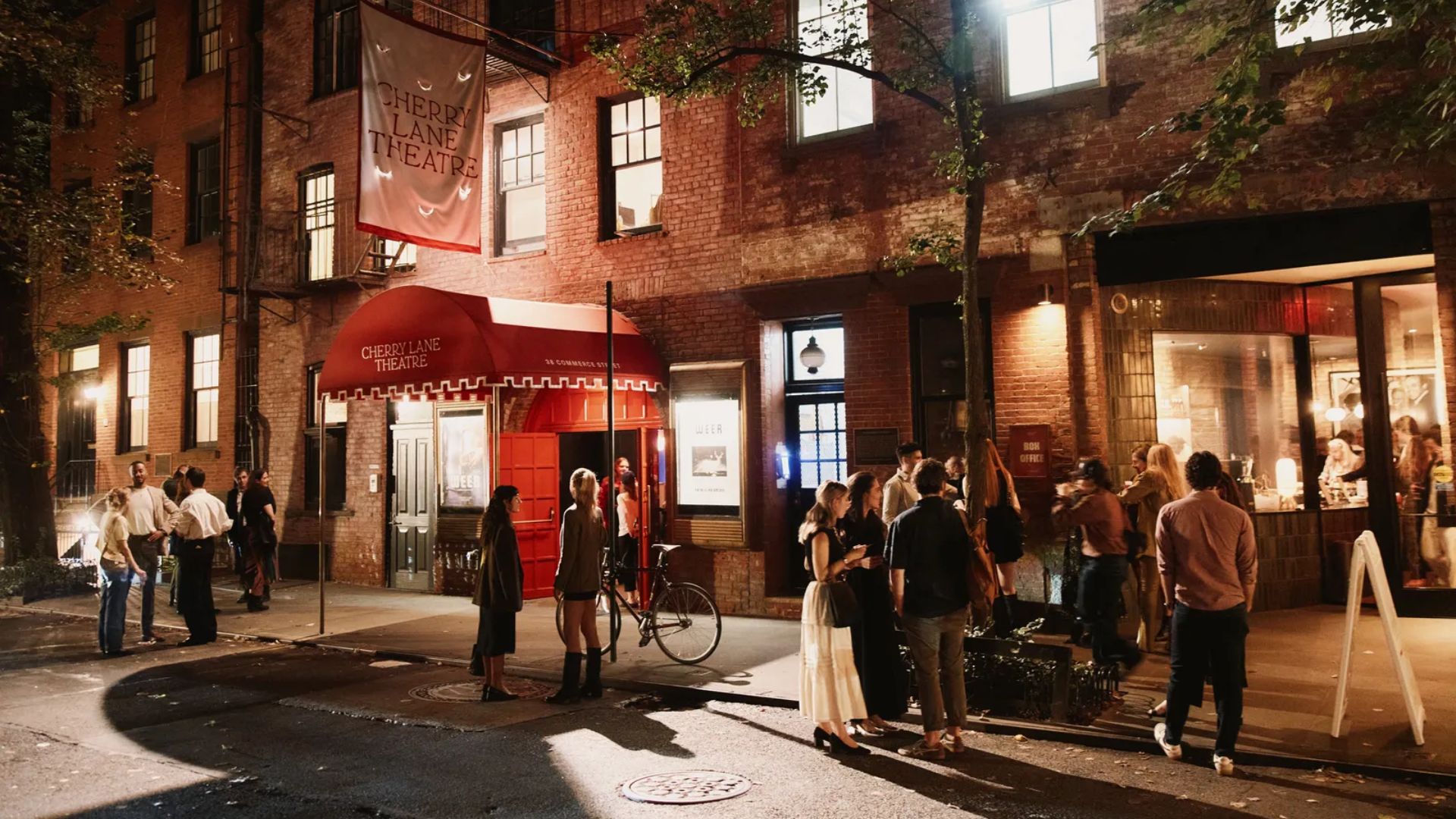 A group of people stands outside a building at night, illuminated by streetlights and the building's exterior lights.