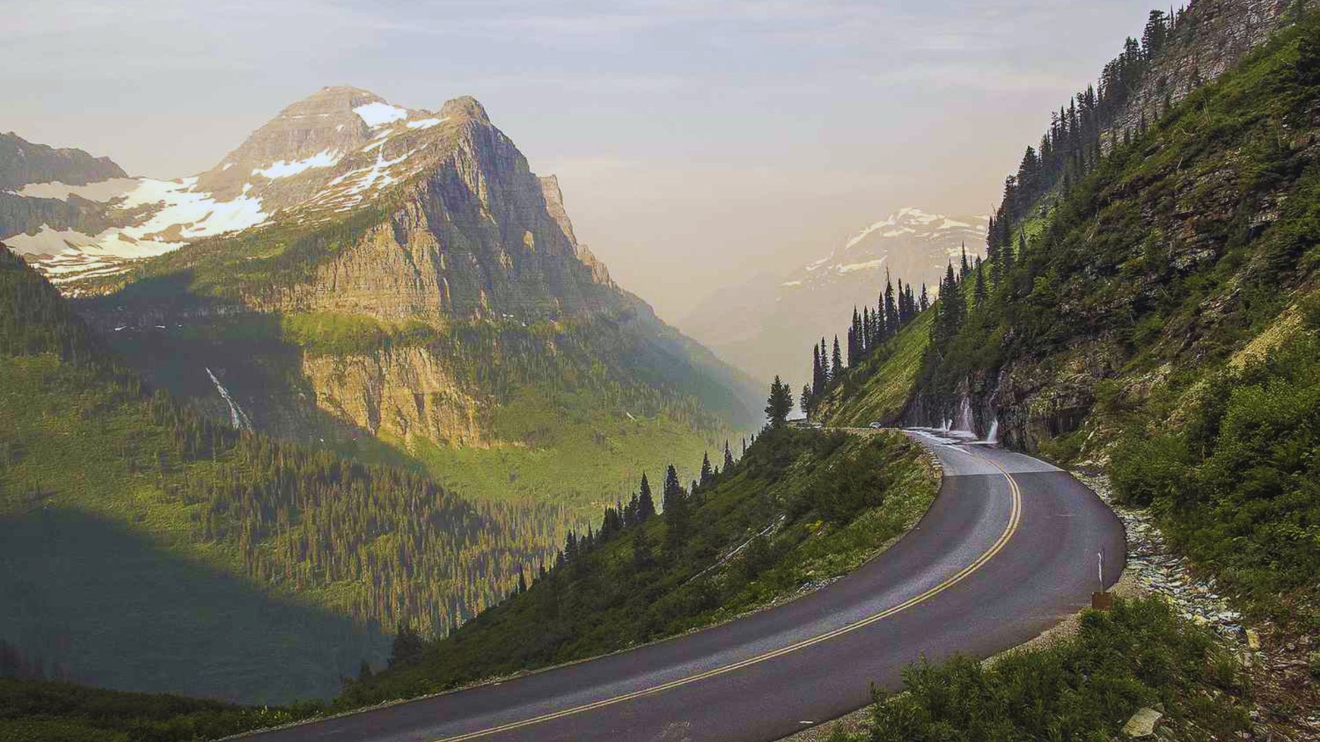 A winding road curves through a scenic mountain landscape, surrounded by lush greenery and rocky peaks.