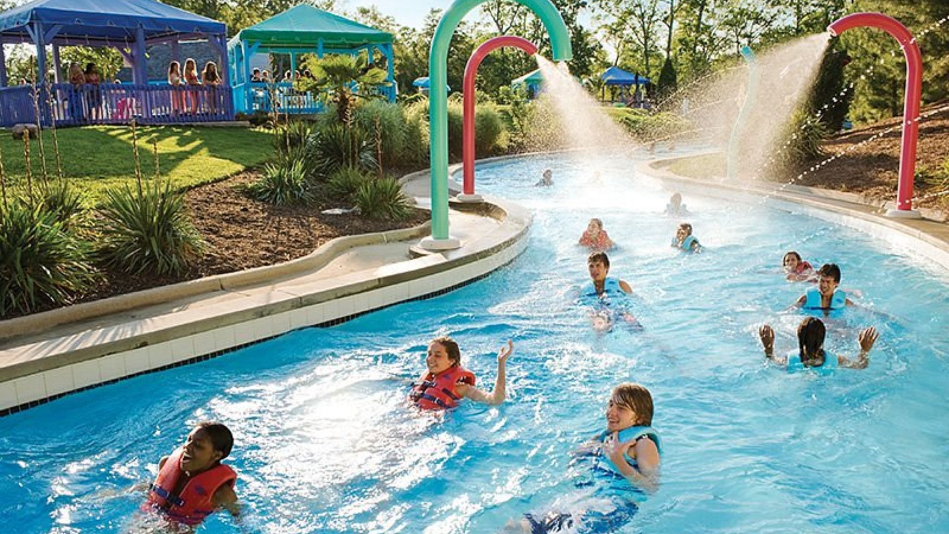 A diverse group of people laughing and splashing water while enjoying a sunny day at a vibrant water park.
