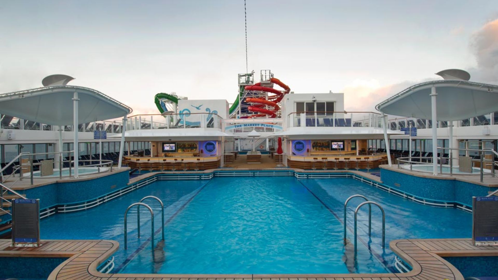 A large swimming pool on a cruise ship, surrounded by sun loungers and deck space for passengers to relax.