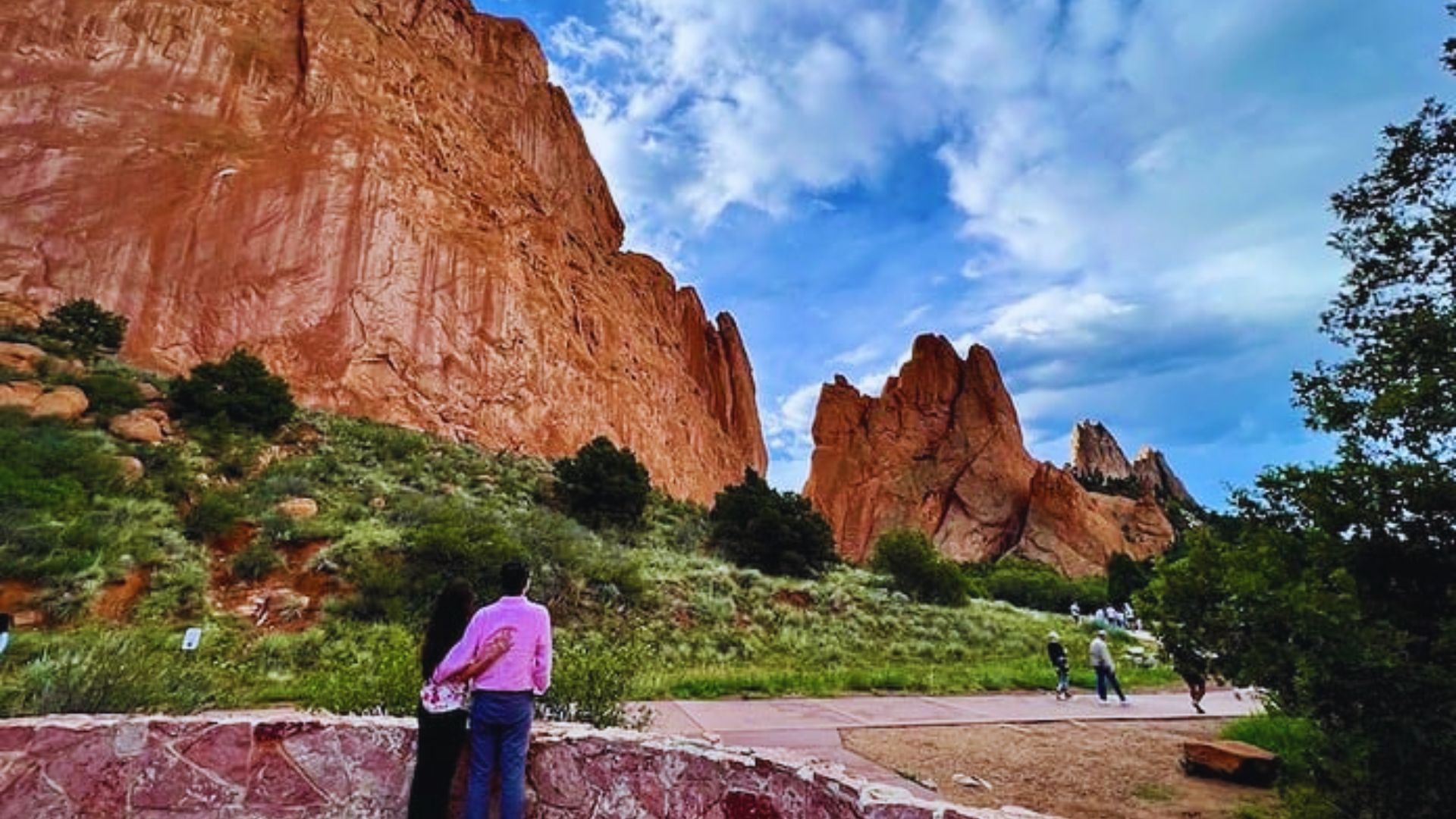 A couple stands on a rock, gazing at a towering rock formation in the background.