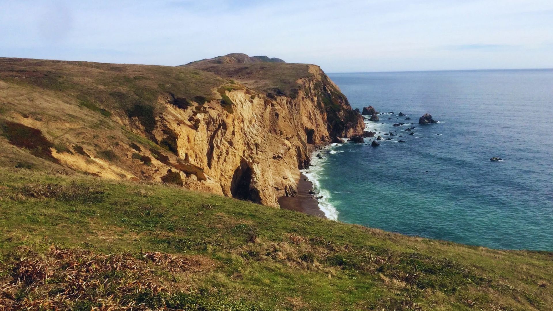 A breathtaking view from a cliff's edge, showcasing the vast ocean stretching to the horizon under a clear blue sky.