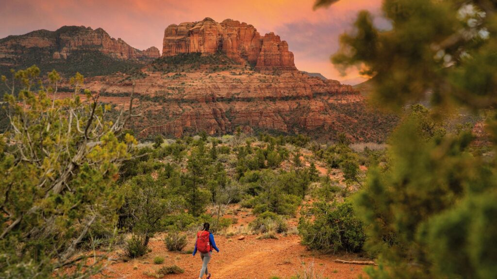 A man strolls on a sandy trail surrounded by arid desert terrain and sparse vegetation.