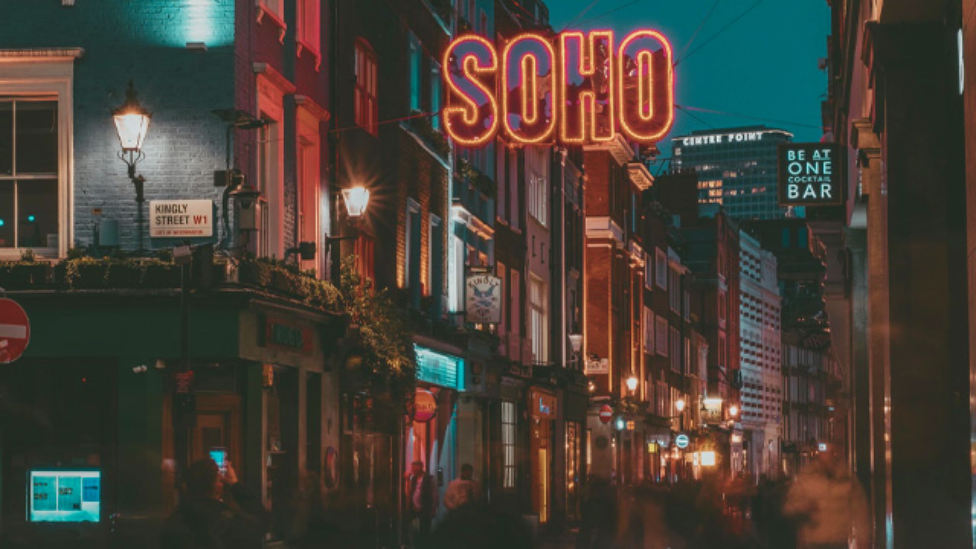 Neon signs illuminate a bustling Soho street in London at night, showcasing the vibrant cityscape and nightlife.