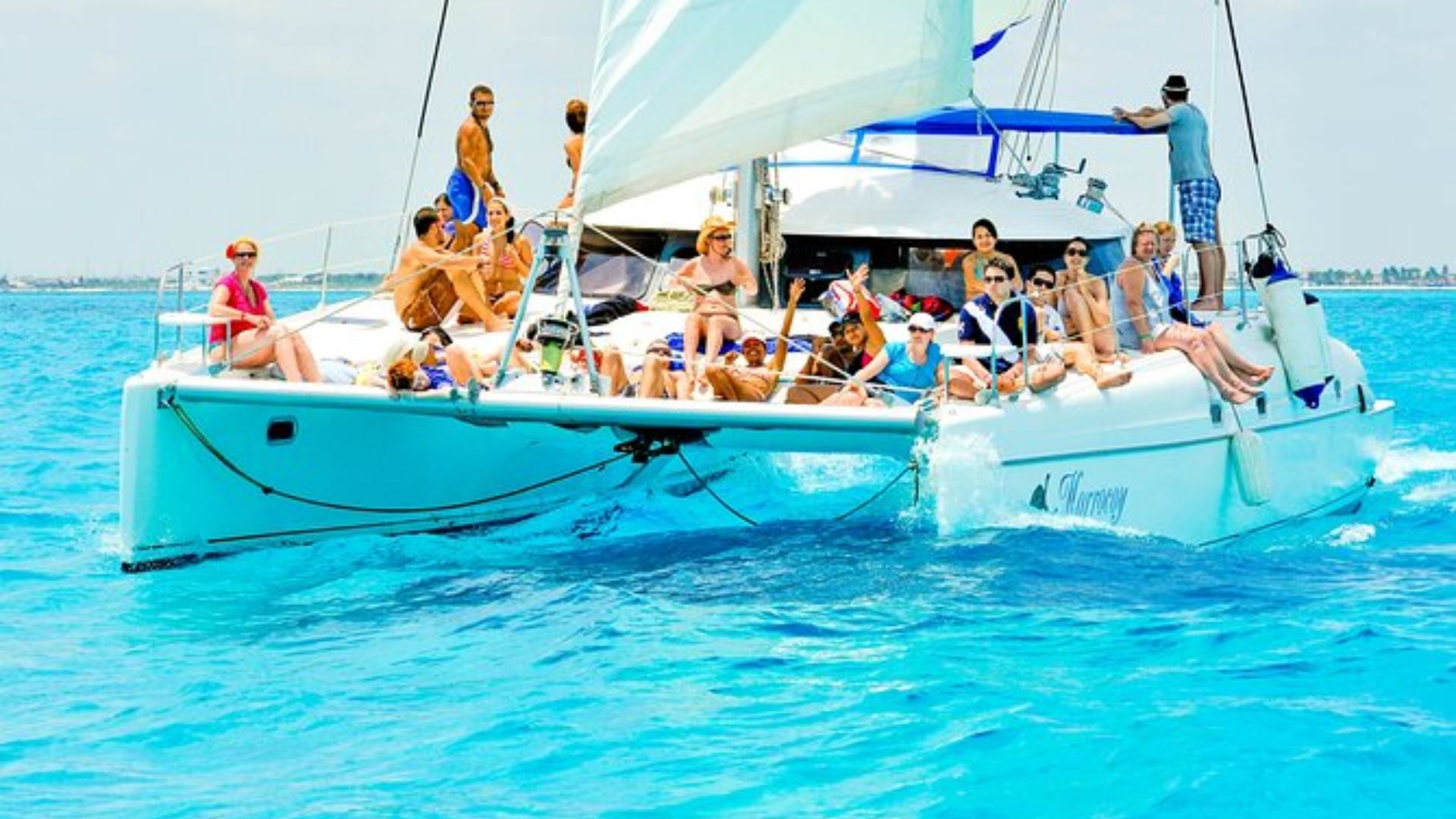 Several individuals aboard a catamaran, surrounded by the vast ocean under a clear blue sky.