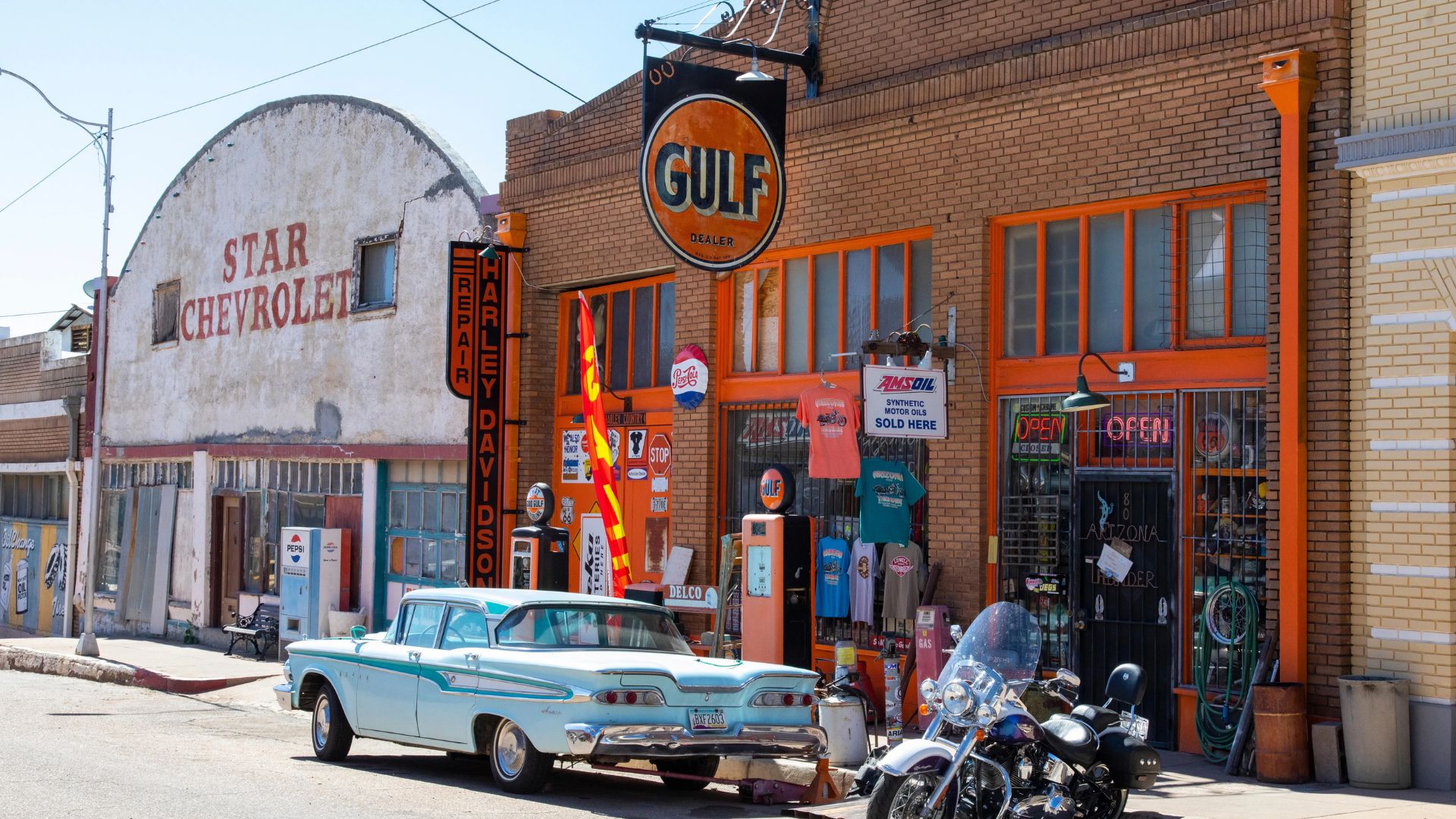 A blue car parked along the street, surrounded by trees and residential buildings.