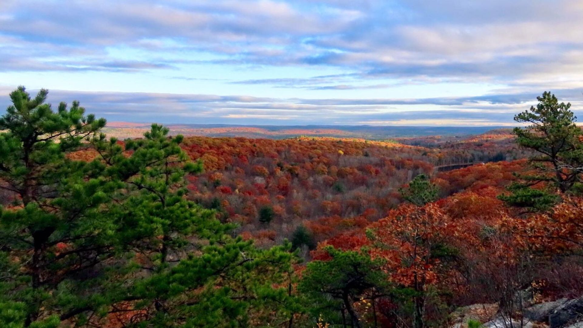 A panoramic view from a mountain peak showcasing vibrant fall foliage and distant valleys under a clear blue sky.