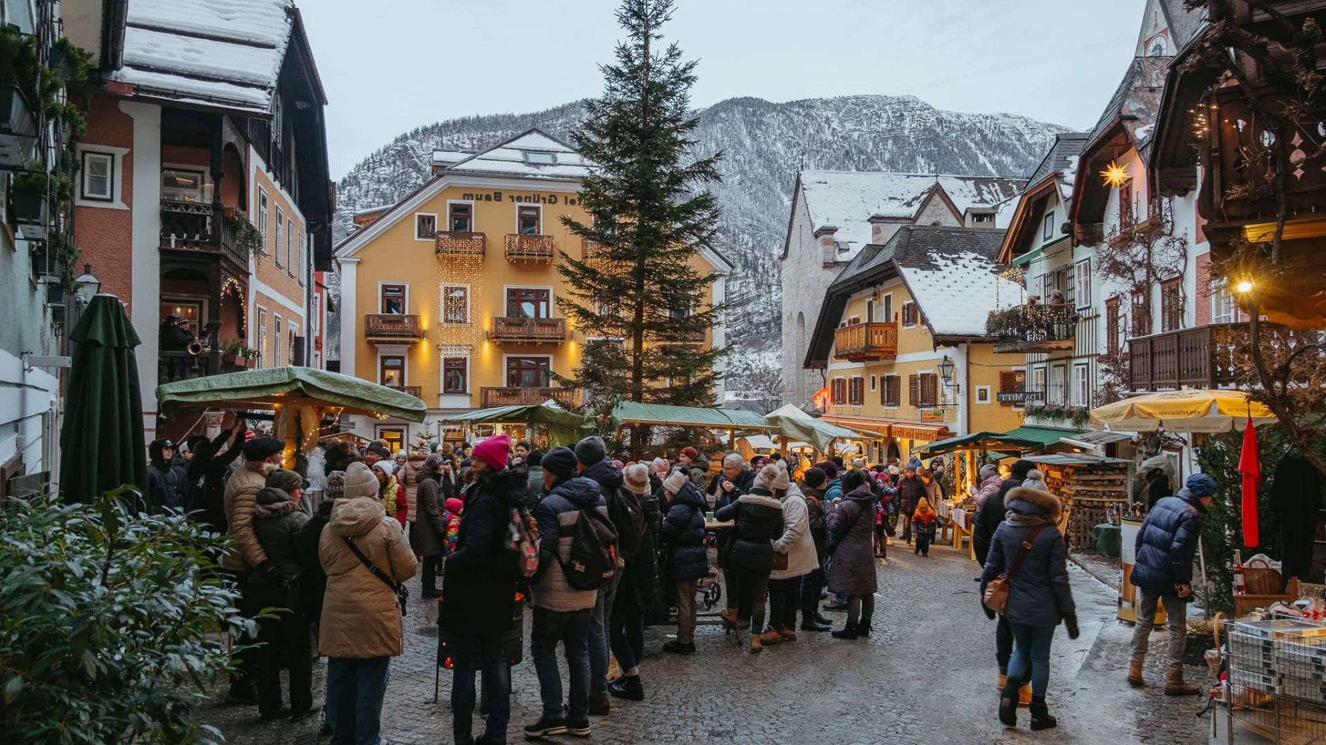 A festive scene of Hallstatt Christmas market, featuring stalls adorned with lights and holiday decorations amidst snowy surroundings.