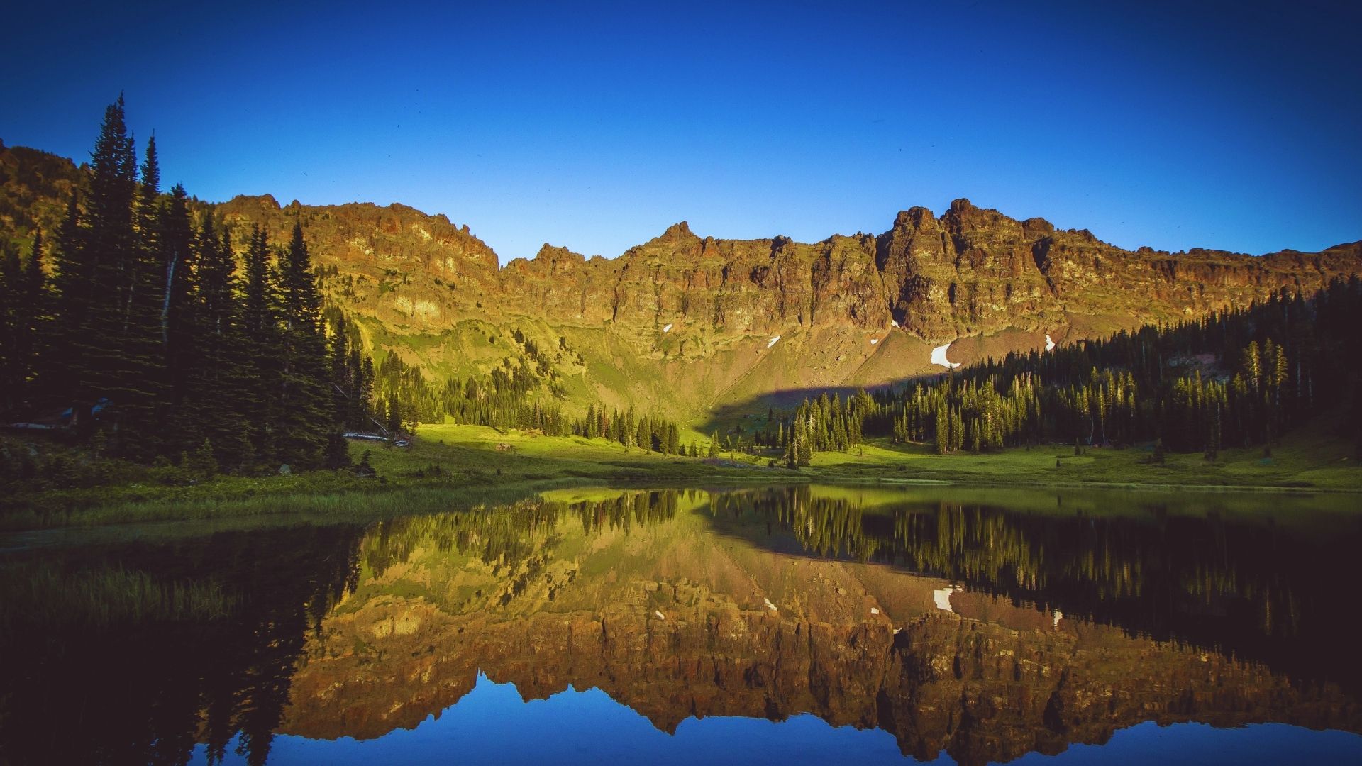 A serene mountain lake reflects the surrounding peaks and sky, creating a tranquil and picturesque scene.