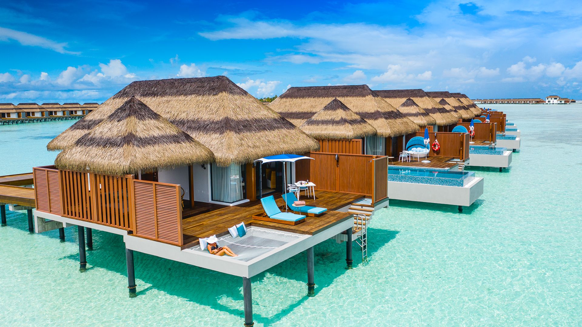 A serene ocean resort featuring thatched huts set on stilts above the water, surrounded by clear blue waves.