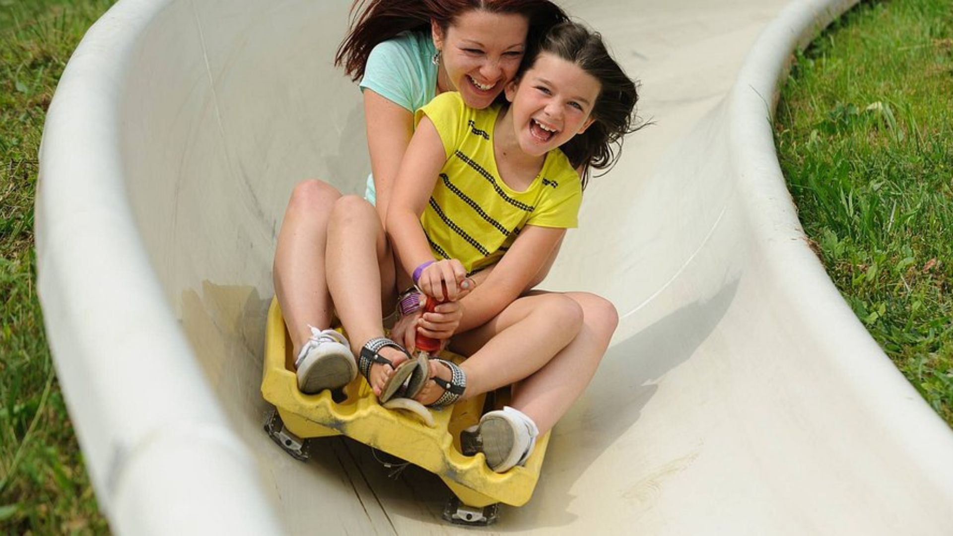 Two young girls joyfully sliding down a playground slide at a park on a sunny day.