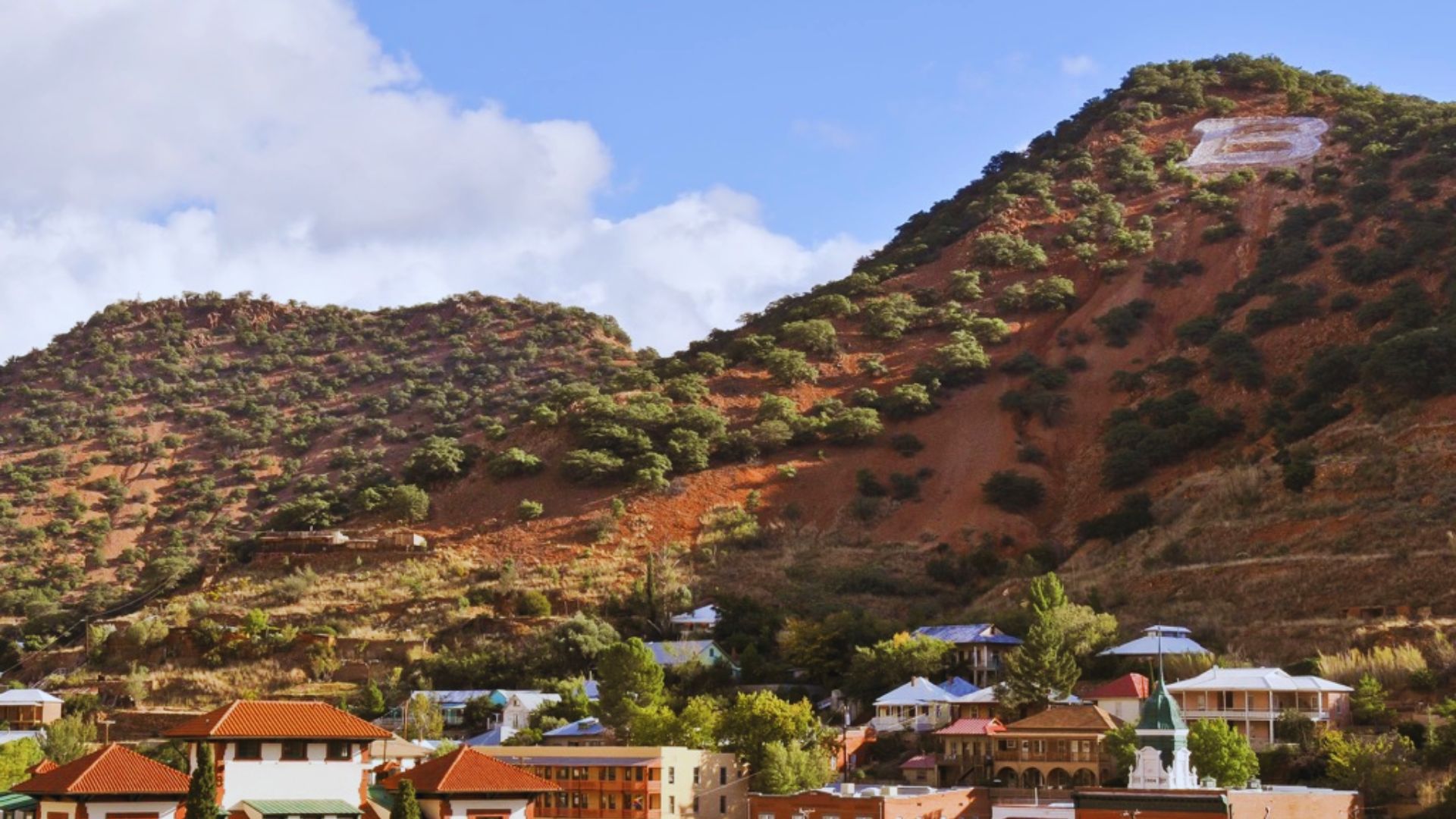 A mountain town with colorful buildings and a prominent sign, nestled against the steep terrain of the mountainside.