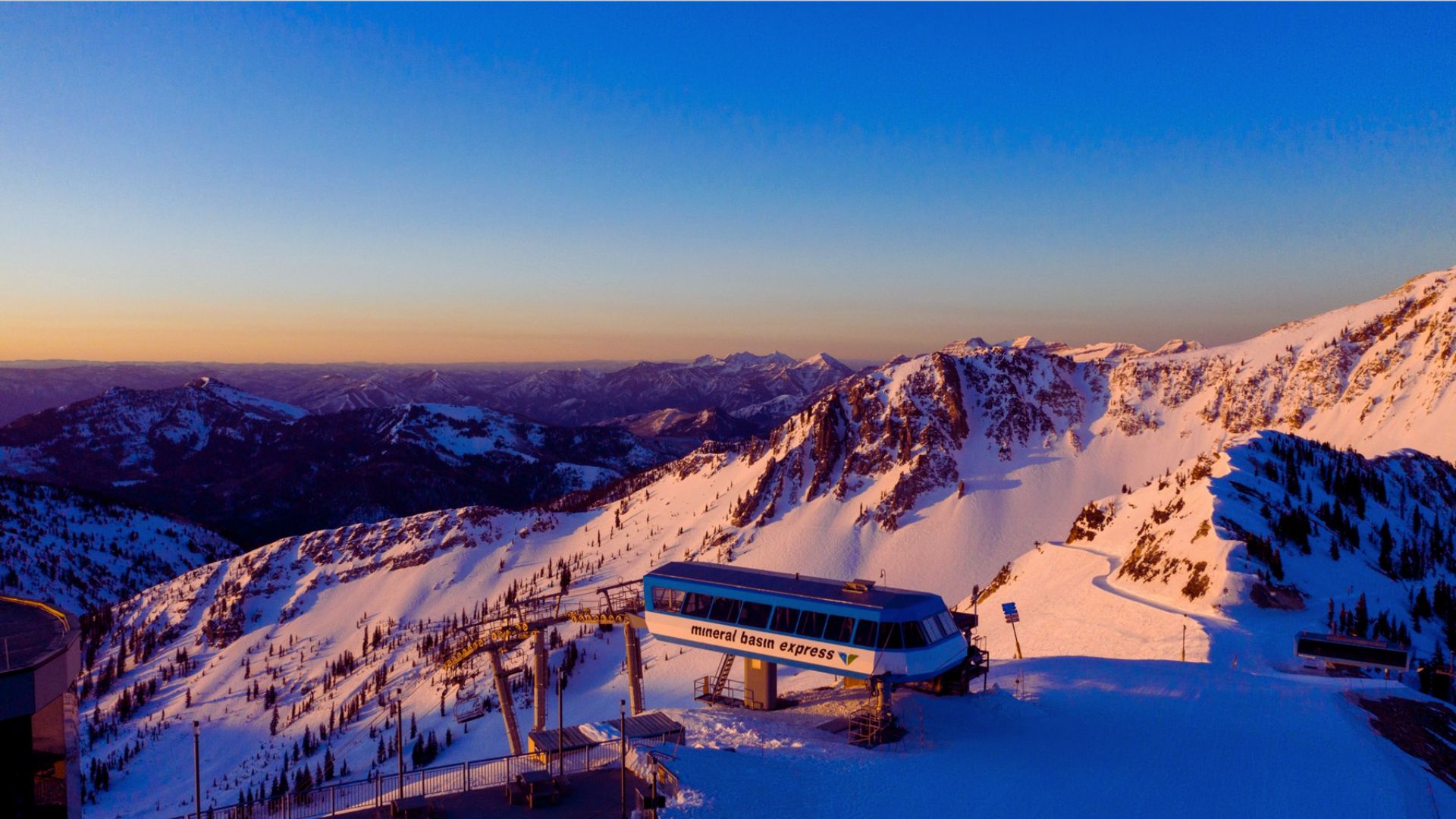 A ski lift overlooking a mountain landscape, illuminated by the colors of sunset.