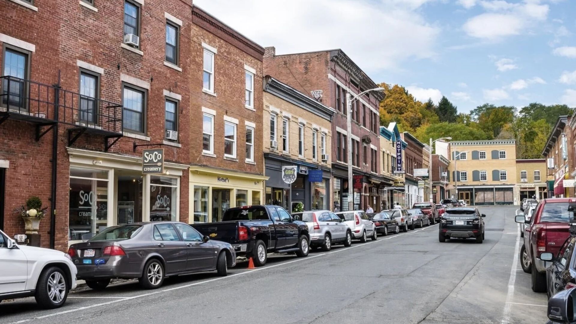 A street view featuring cars parked on both sides, creating a narrow passage for pedestrians and other vehicles.