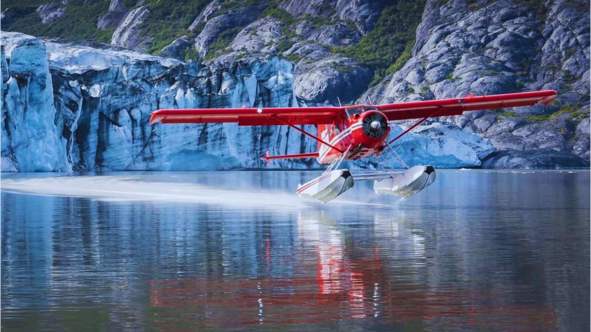 A red sea plane soars above a stunning glacier, showcasing the contrast between the vibrant aircraft and icy landscape.