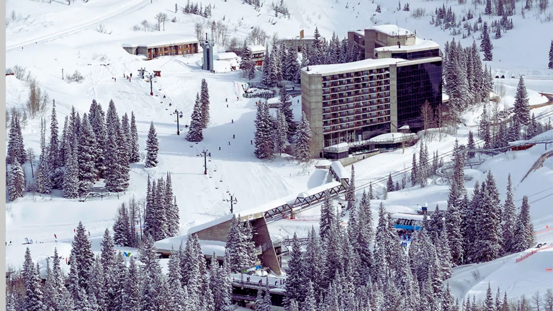 A ski resort featuring a ski lift and a hotel surrounded by snow-covered mountains and pine trees.