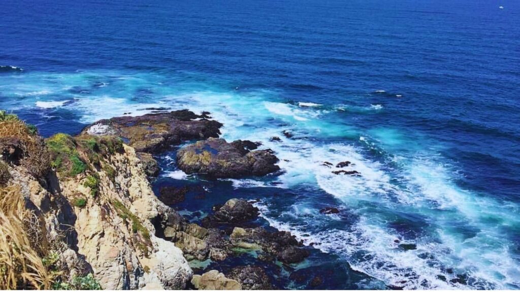 A vibrant blue ocean contrasts with rugged, rocky cliffs under a clear sky.