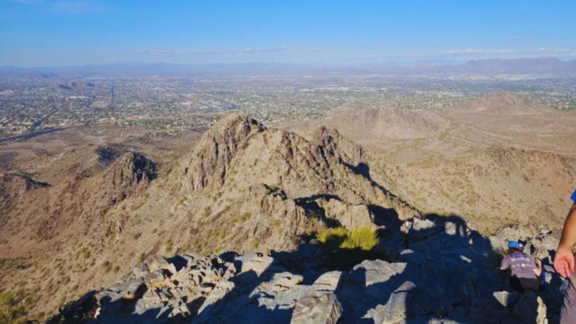 A man stands triumphantly on a mountain peak, overlooking a vast landscape below.