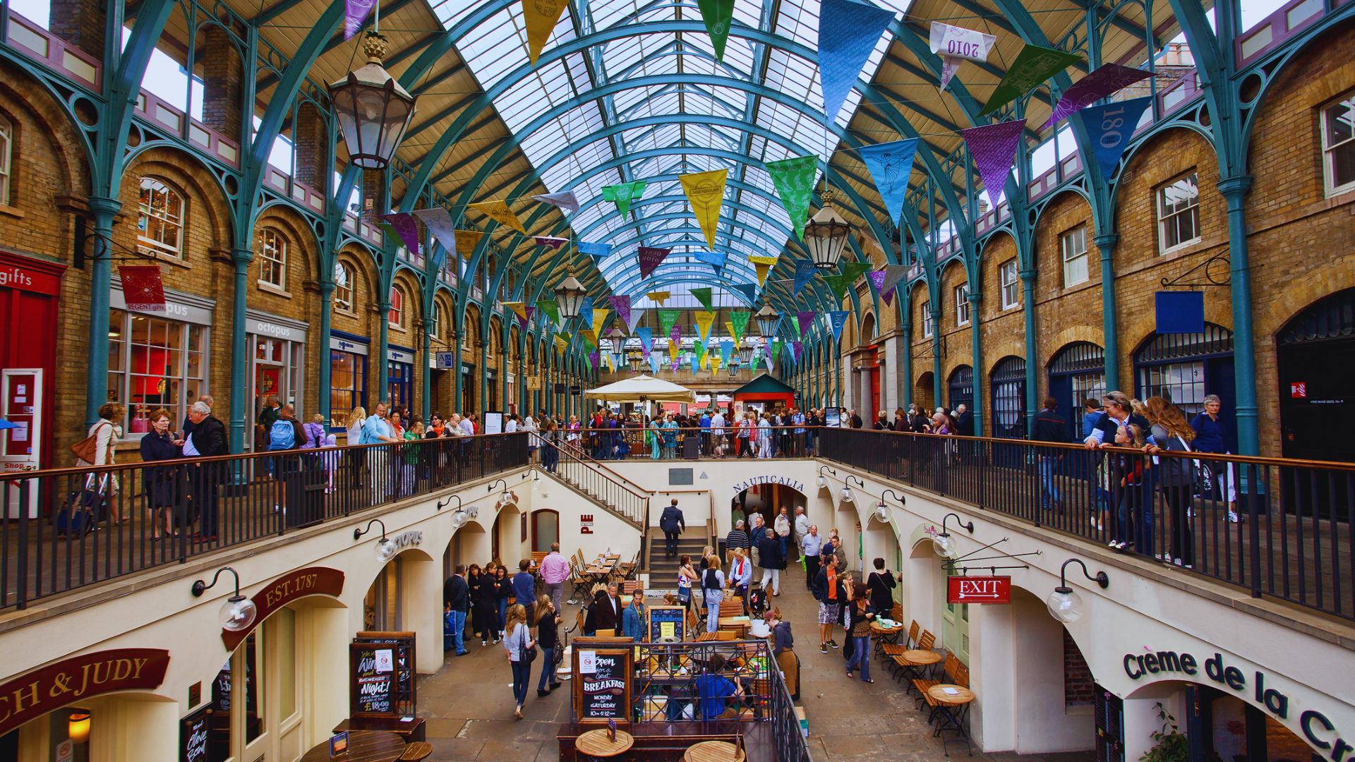 A bustling indoor market filled with people browsing stalls and walking through the aisles.