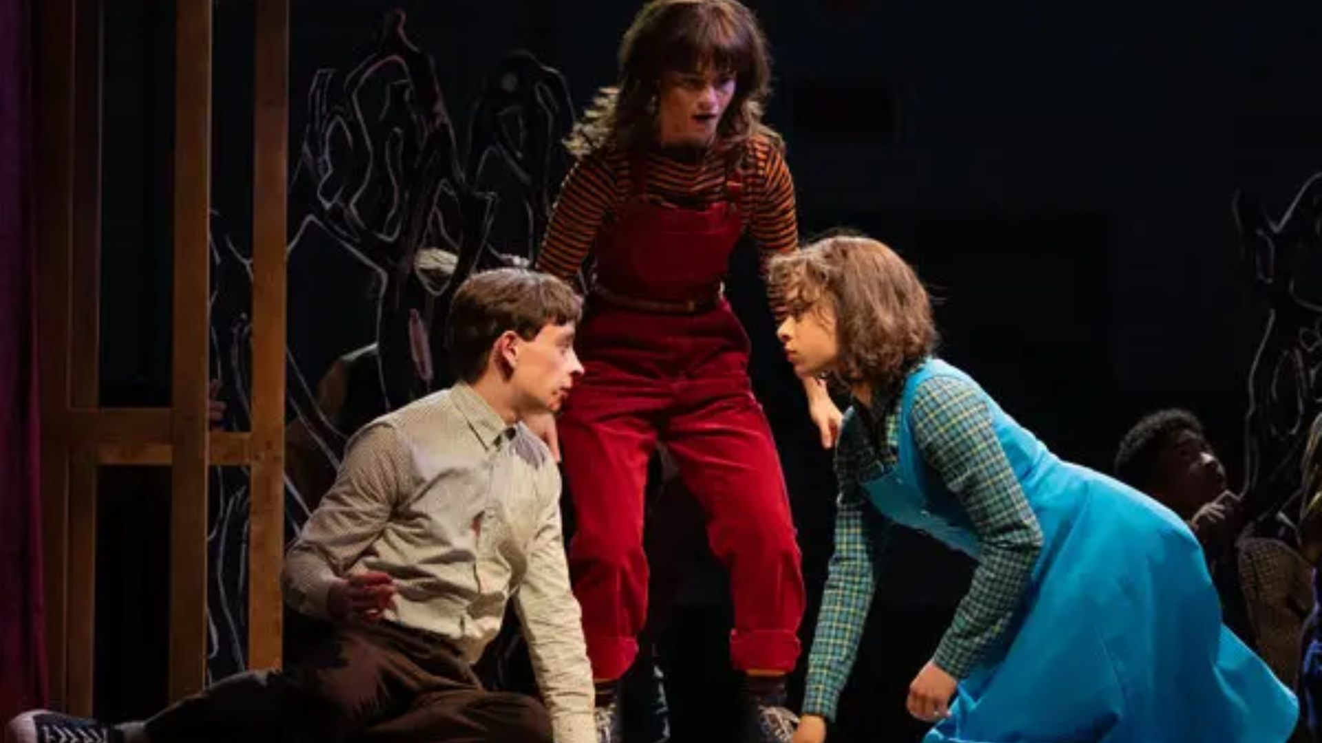 Three actors performing on stage in a musical, captivating the audience with their energetic presence and colorful outfits.