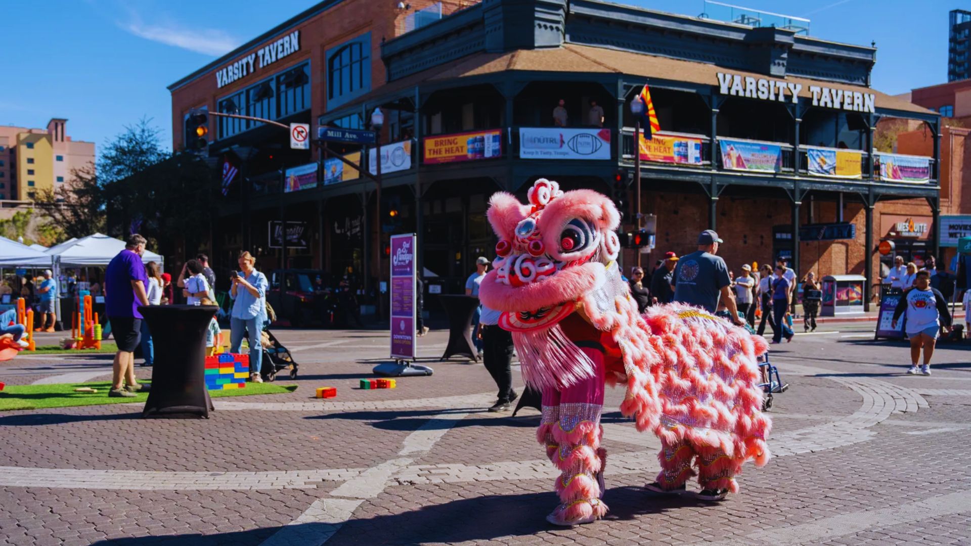 A pink lion casually walks down the street, contrasting with the typical scenery of a city.