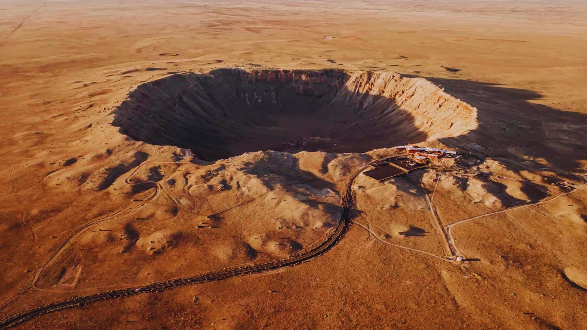 Overhead perspective of a vast crater in the desert, highlighting its depth and the arid landscape around it.