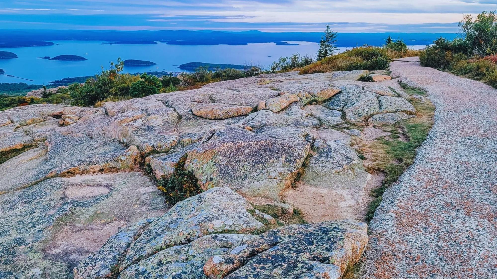 A winding path leads to a mountain top, surrounded by rocks and a flowing stream of water.