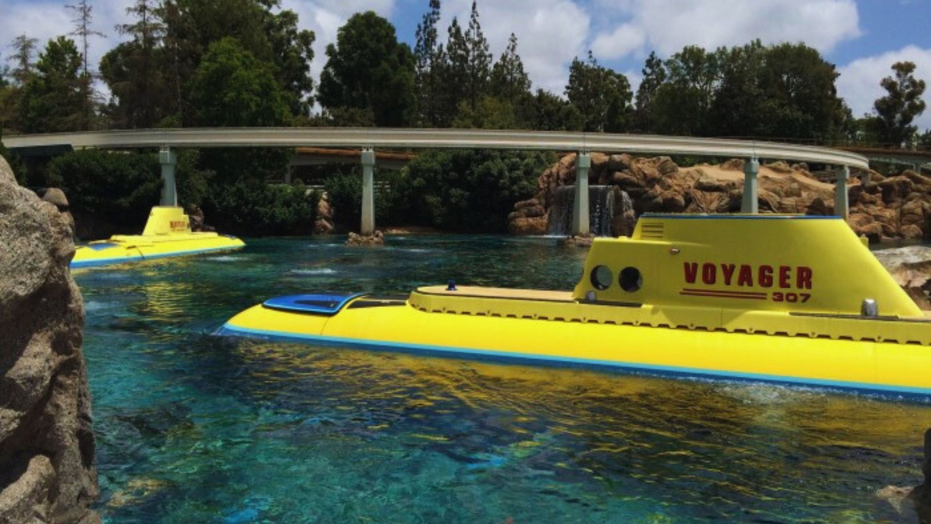 A bright yellow submarine floats in the water at a vibrant water park, surrounded by playful splashes and attractions.