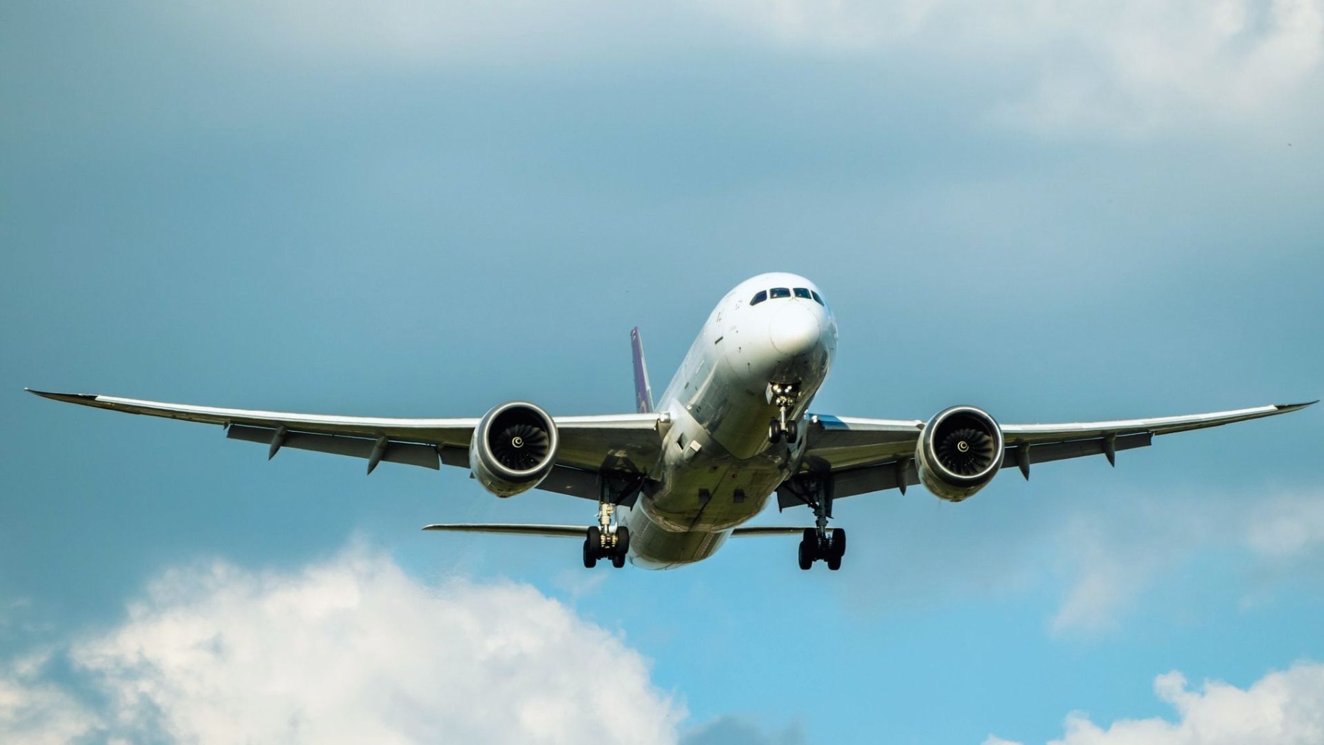A large passenger jet soaring through a clear blue sky, showcasing its wings and fuselage against the backdrop of clouds.