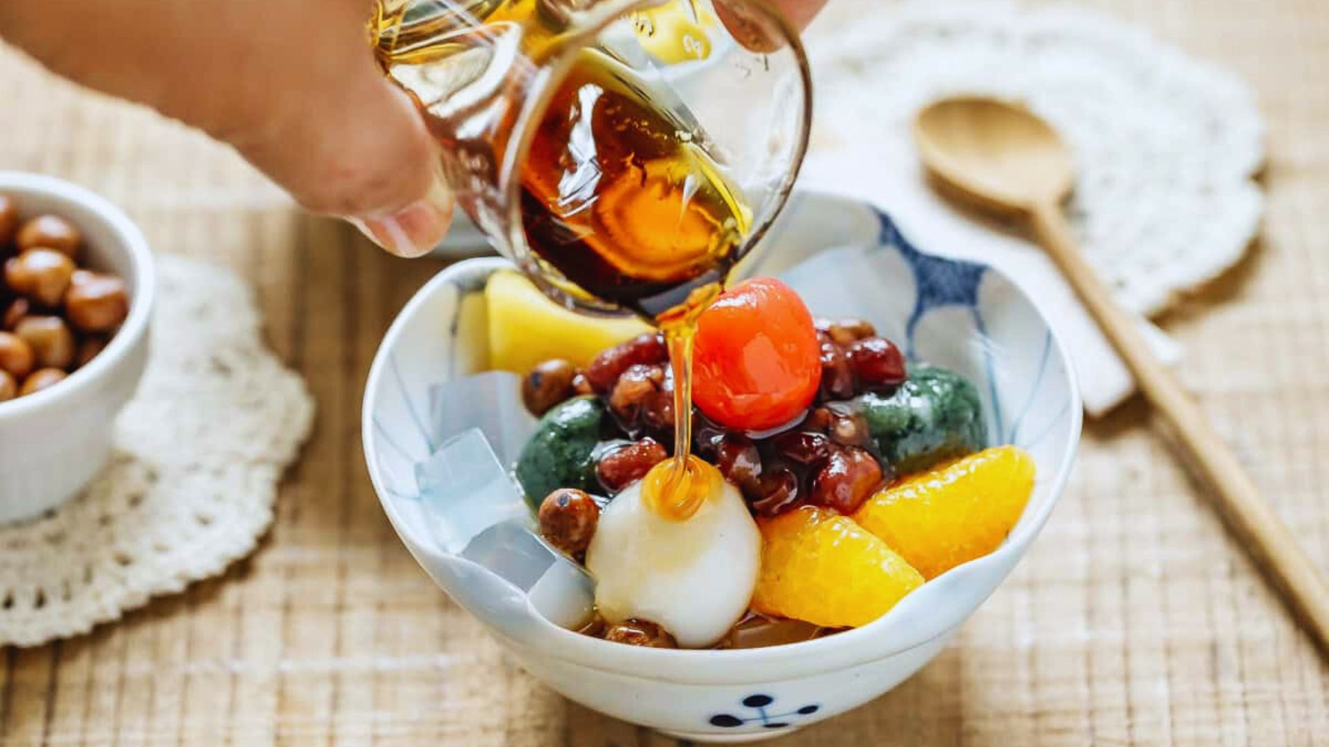 Syrup is being poured over a bowl of mixed fruit and nuts.