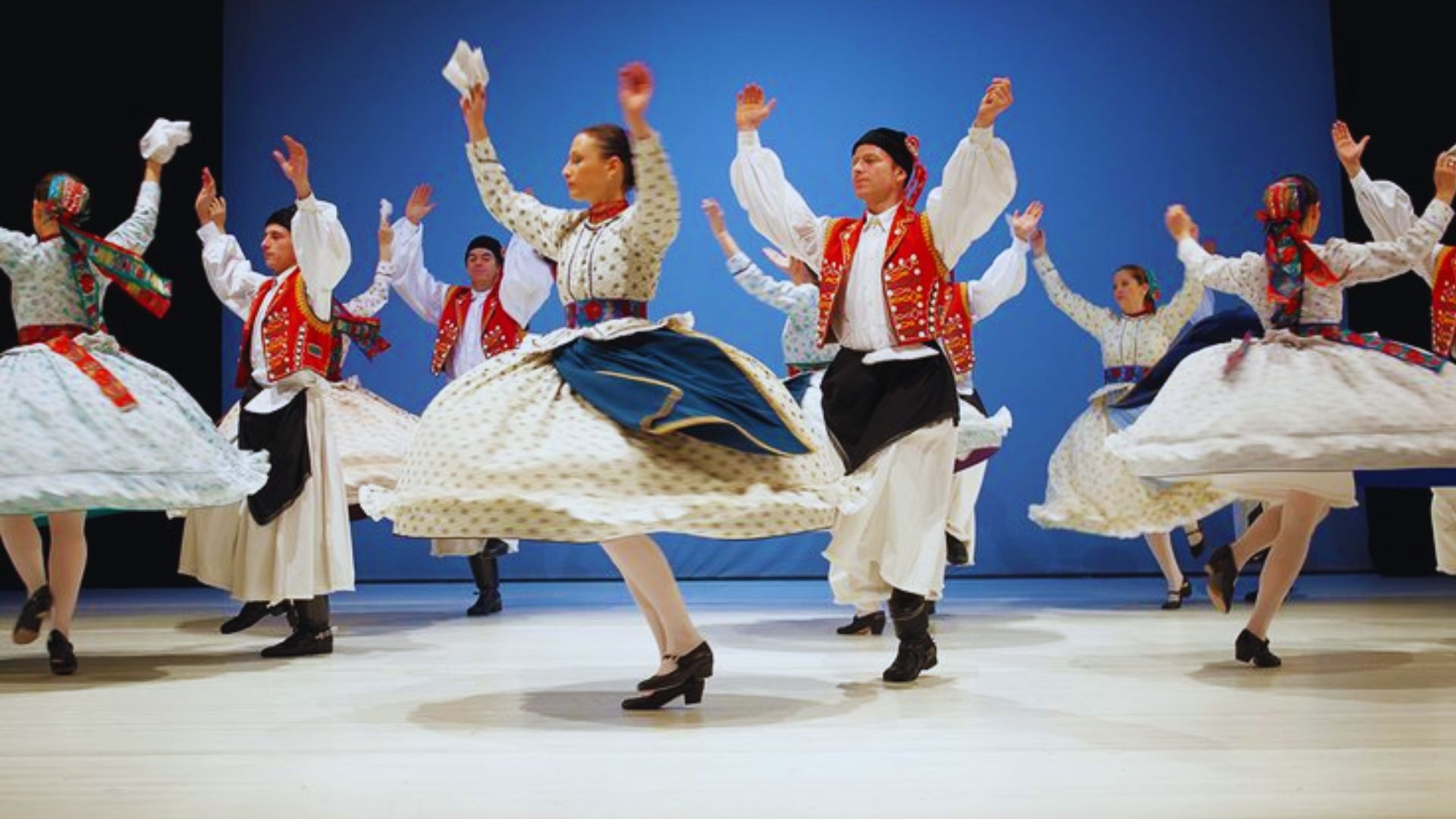 A group of people in colorful traditional costumes joyfully dancing together in a festive outdoor setting.