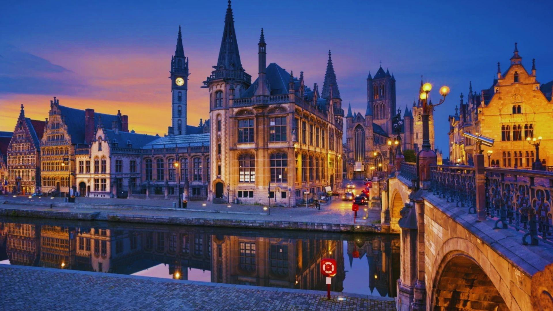 The city of Bruges illuminated at dusk, showcasing its historic architecture and serene canals under a twilight sky.