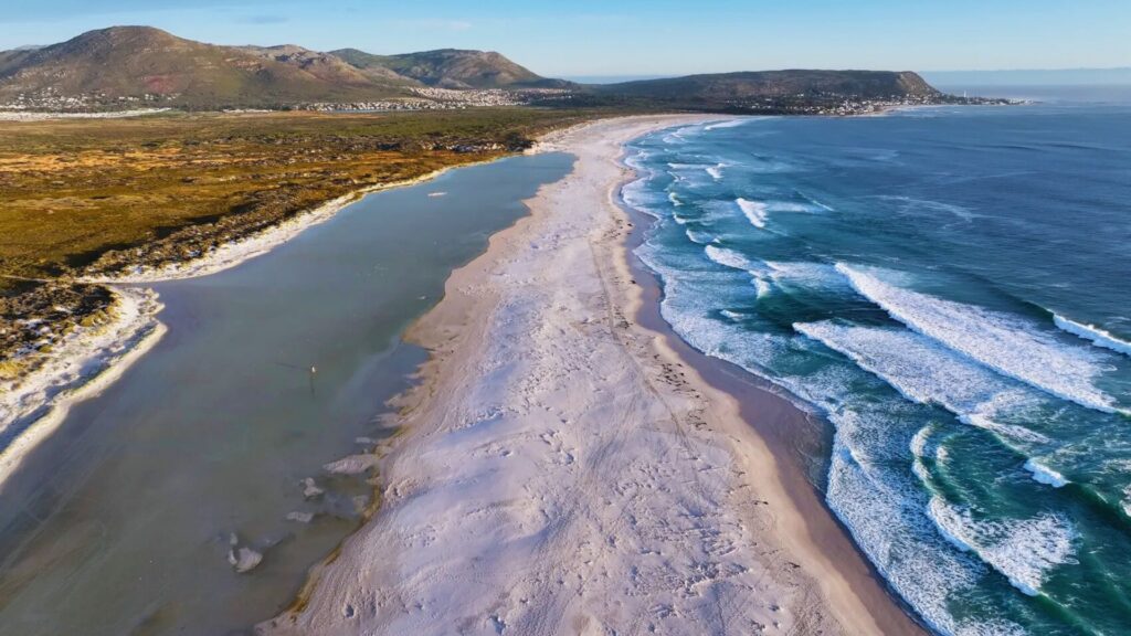 17 Best Beaches in South Africa for Adventure & Relaxation Aerial view showcasing a sandy beach bordered by lush mountains under a clear blue sky.