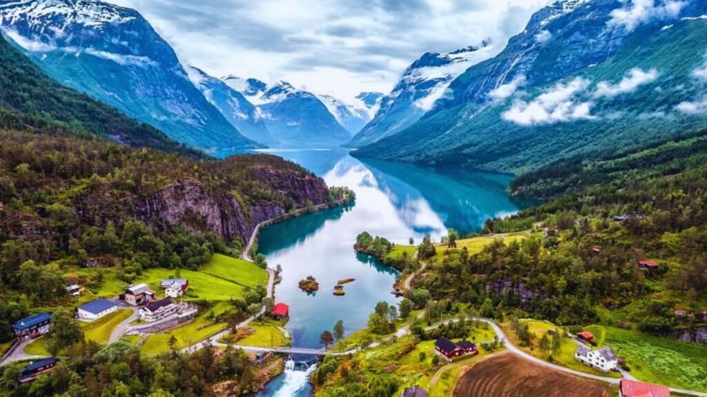 Scenic Norwegian landscape featuring a serene lake surrounded by majestic mountains under a clear blue sky.