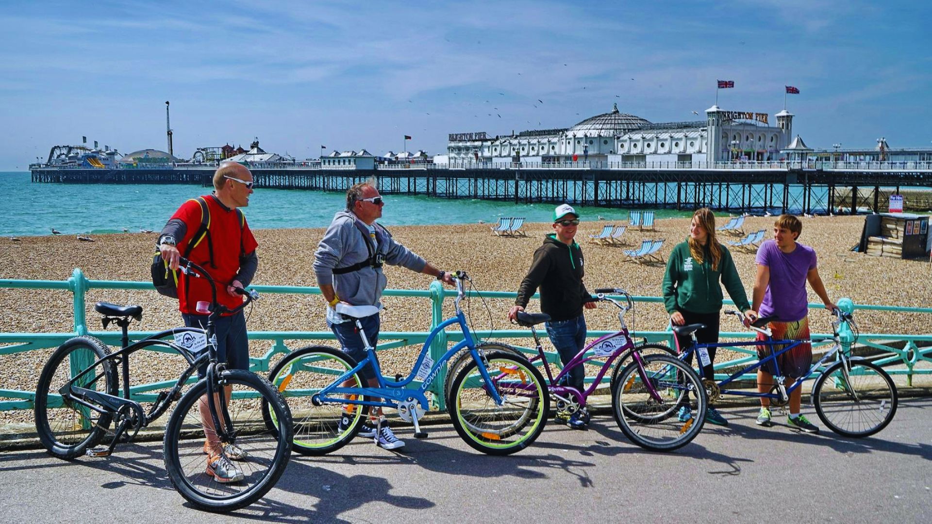 A group of people with bicycles enjoying a sunny day on the beach, surrounded by sand and ocean waves.
