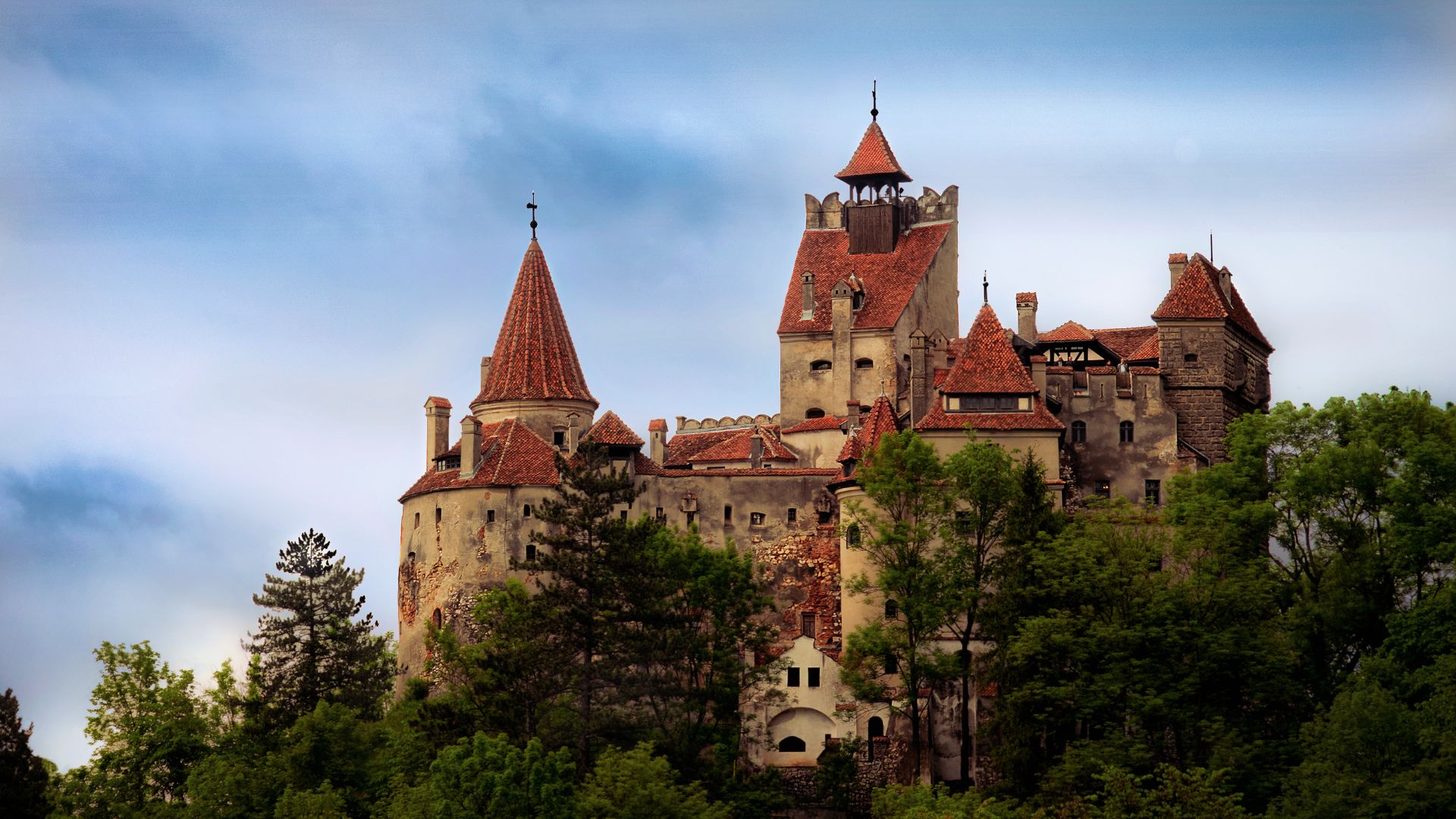 Bran Castle in Romania, a historic fortress surrounded by lush green hills and a clear blue sky.