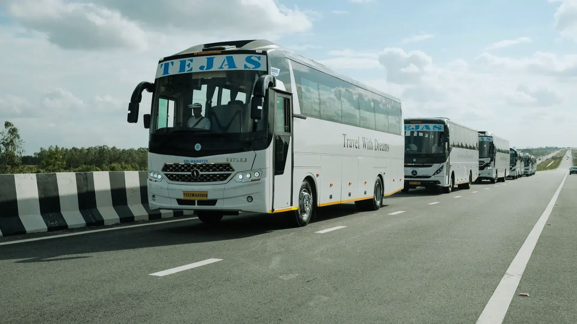 Multiple buses on the road against a backdrop of blue sky.