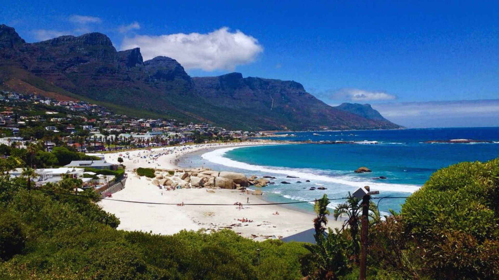 . Scenic view of Cape Town beach, featuring golden sand, clear blue water, and Table Mountain in the background.