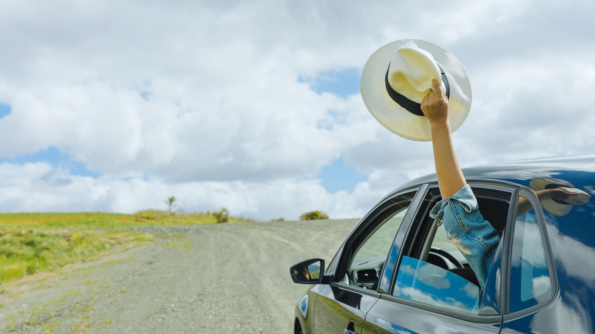 A woman wearing a hat drives her car along a scenic road, focused on the journey ahead.