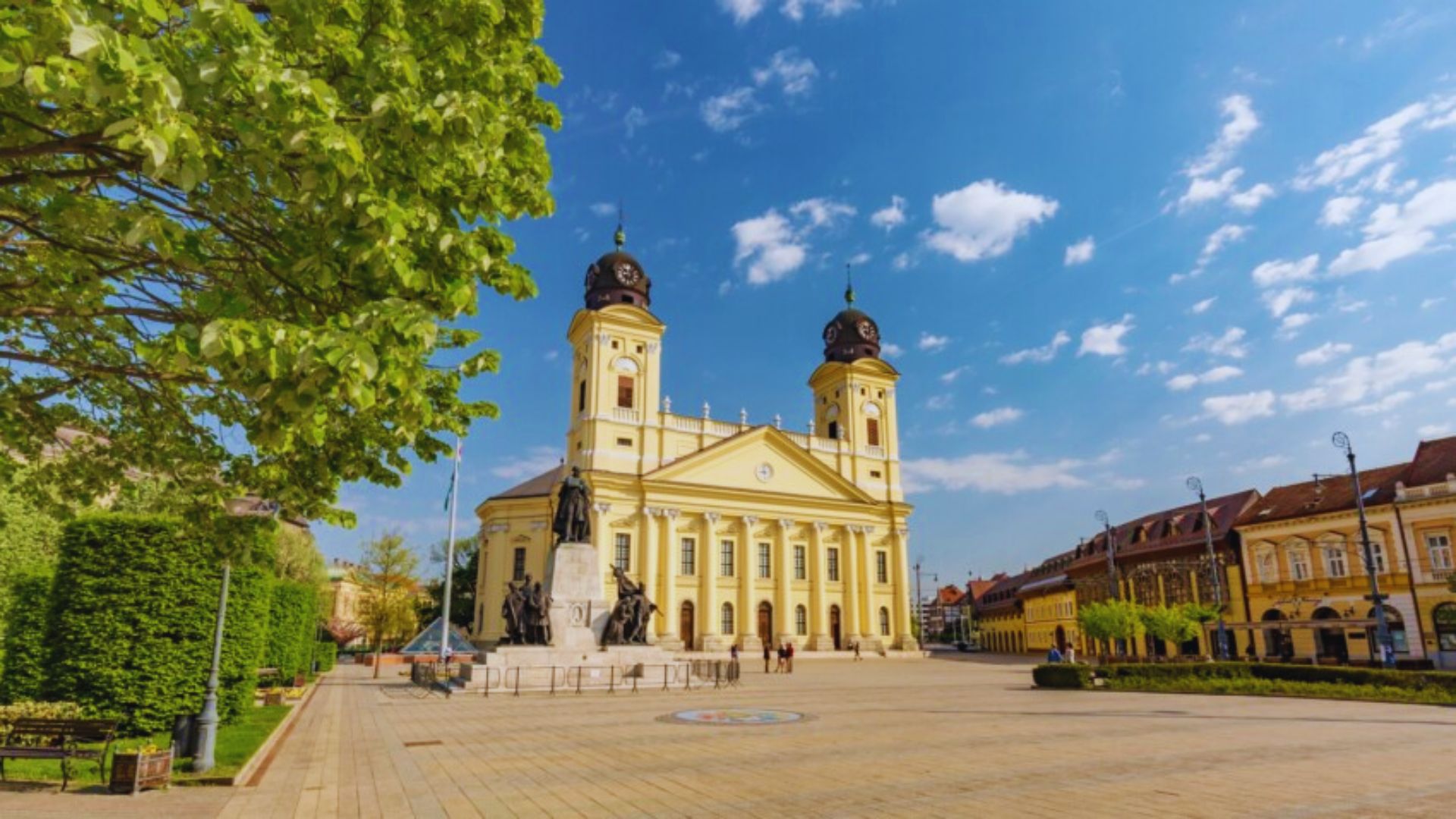 A grand cathedral stands prominently in the center of a bustling town square, surrounded by people and shops.