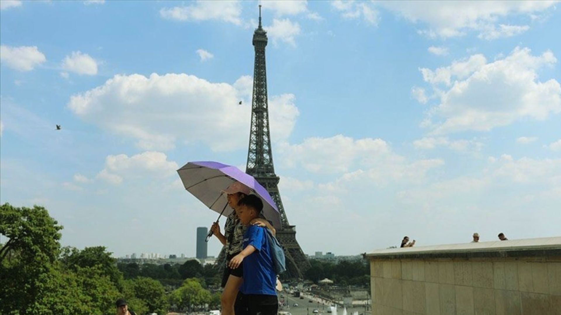 A couple stands under an umbrella, smiling in front of the Eiffel Tower on a rainy day.