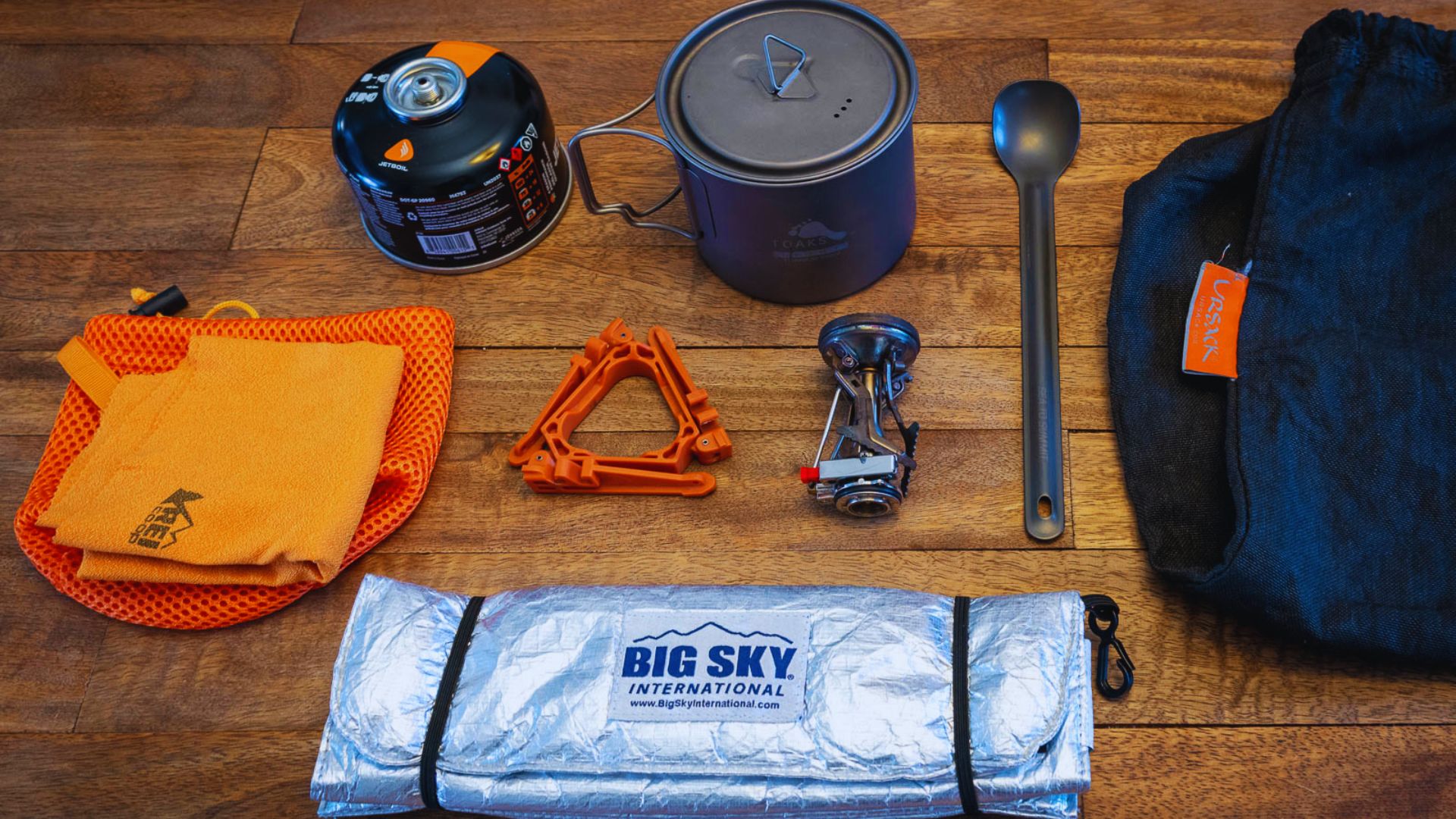 A backpack's contents, including books and supplies, are spread out on a wooden floor for easy viewing.