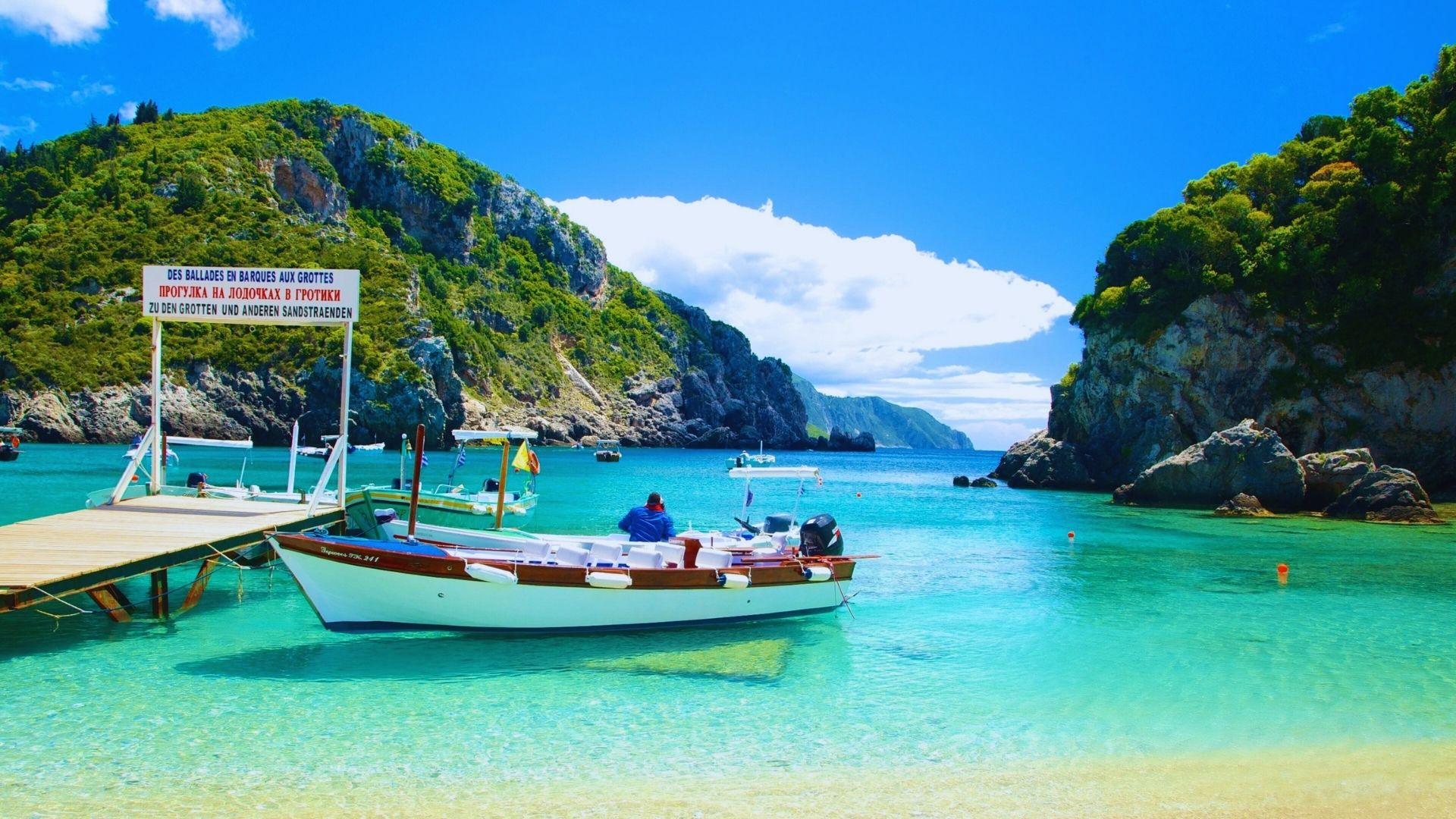 A boat is docked at a sandy beach with clear, turquoise water gently lapping at the shore.