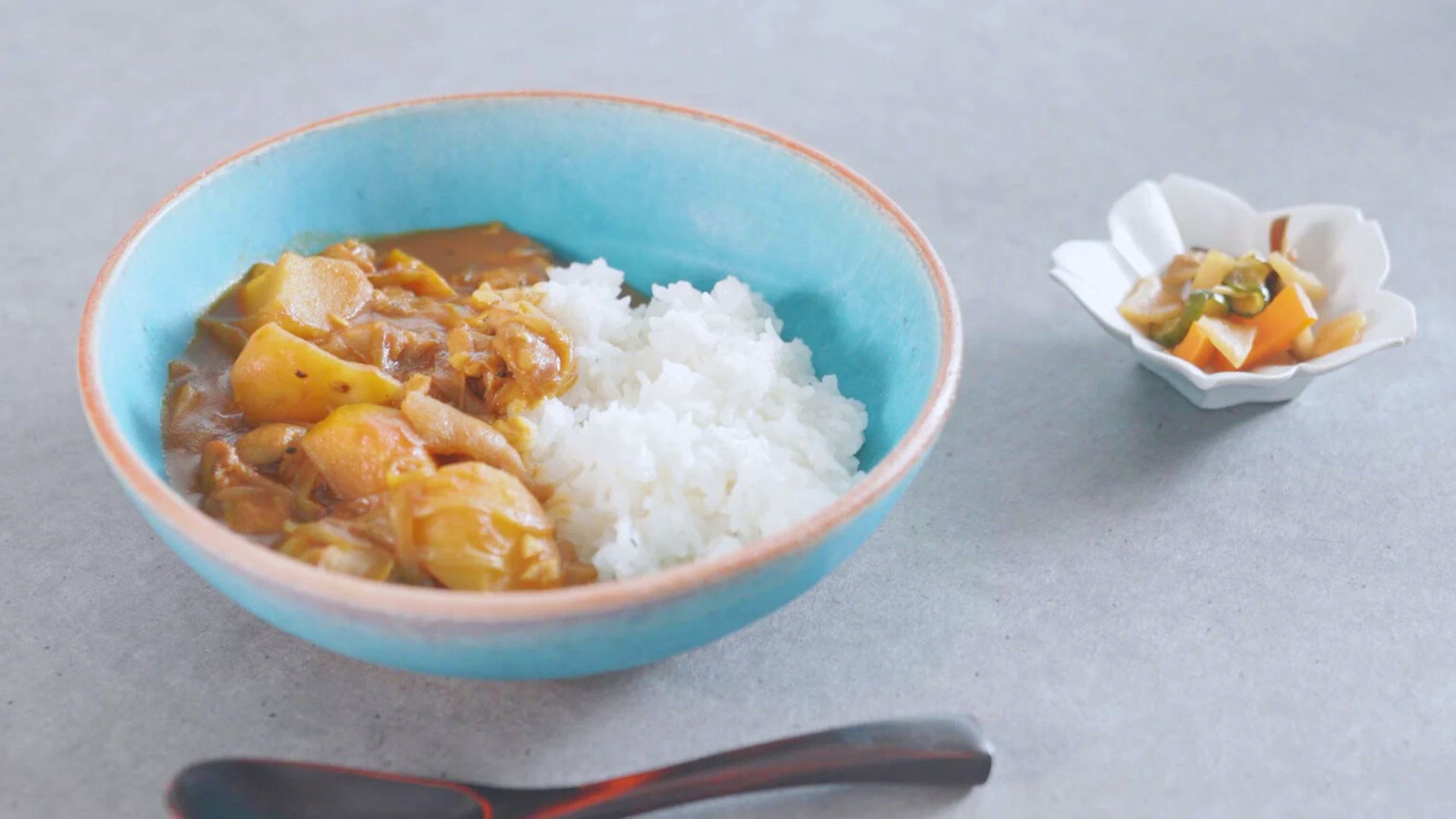 A bowl filled with curry and rice, accompanied by a spoon on the side.